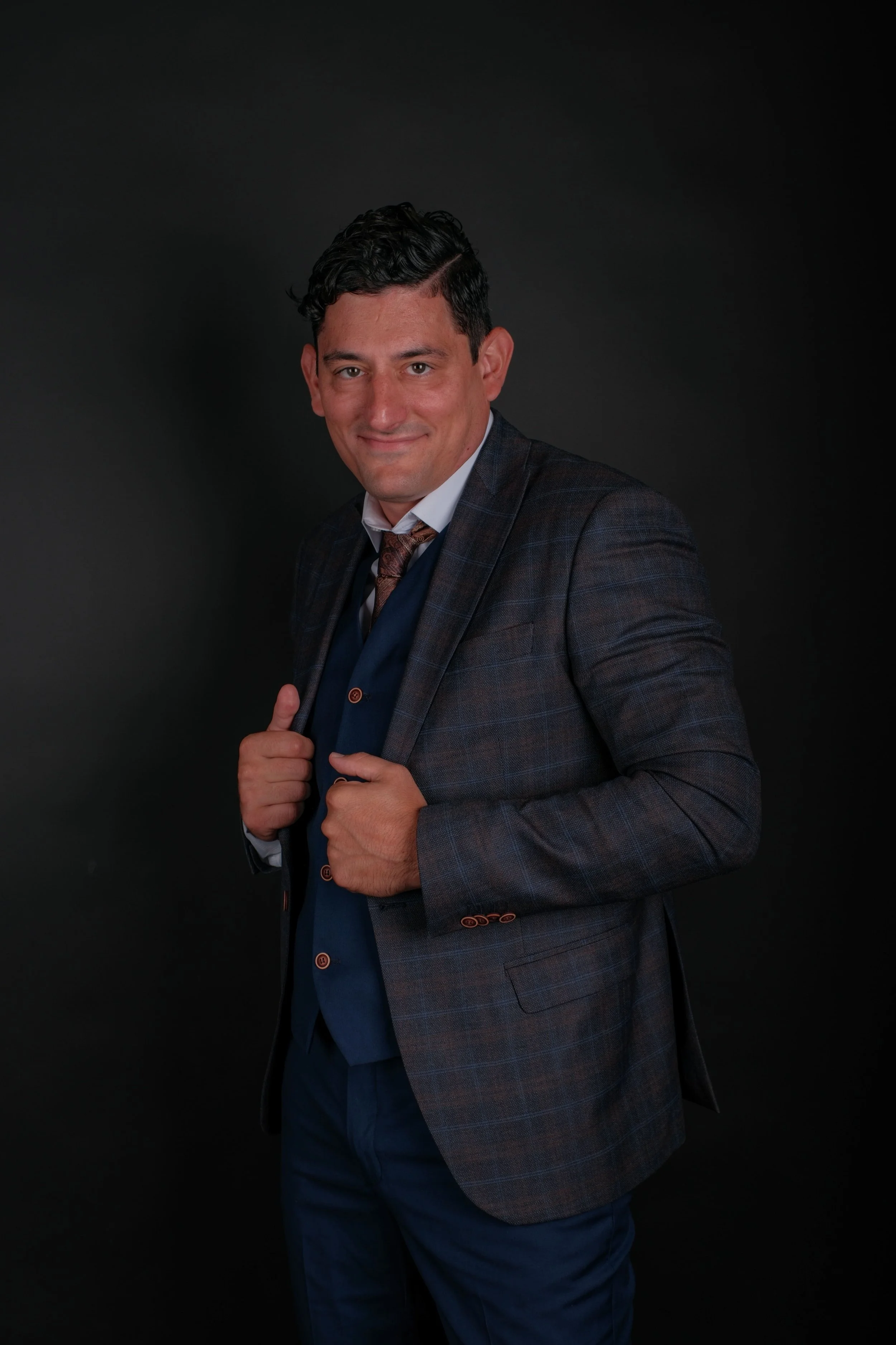 Author Alex Rodino posing in a professional studio portrait wearing a navy suit and plaid blazer.