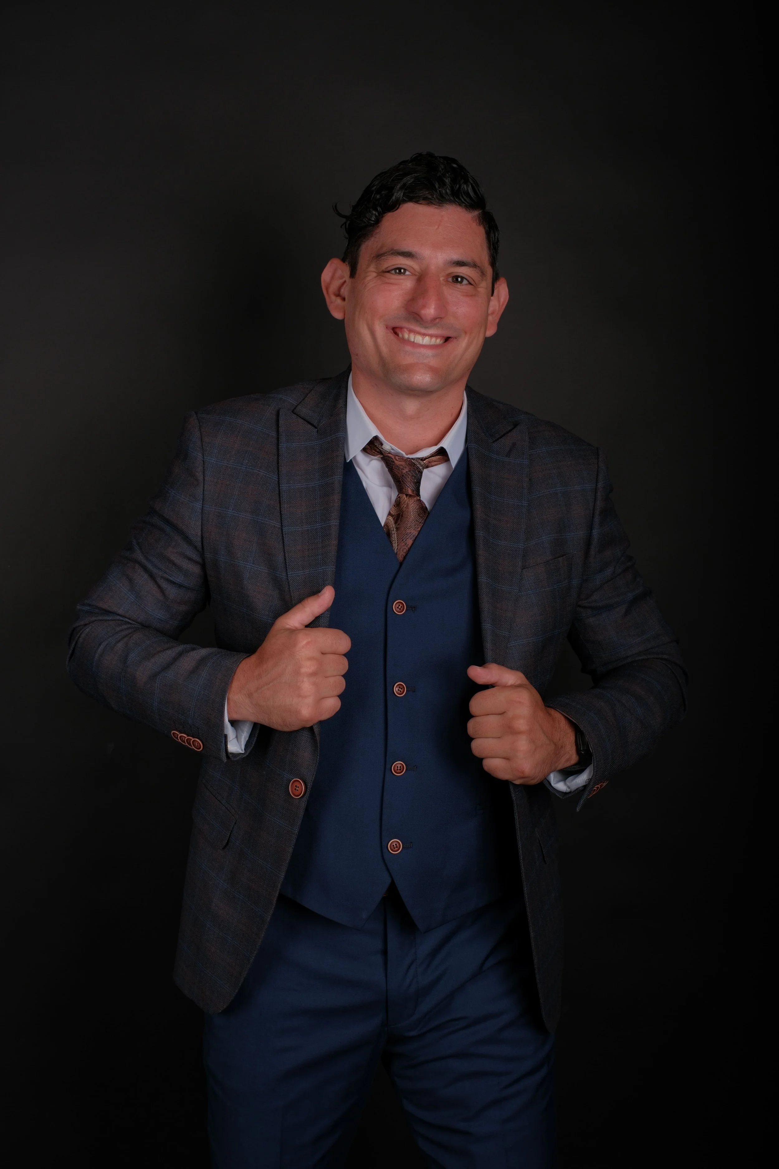 Alex Rodino smiling in a professional studio portrait wearing a navy suit and plaid blazer.