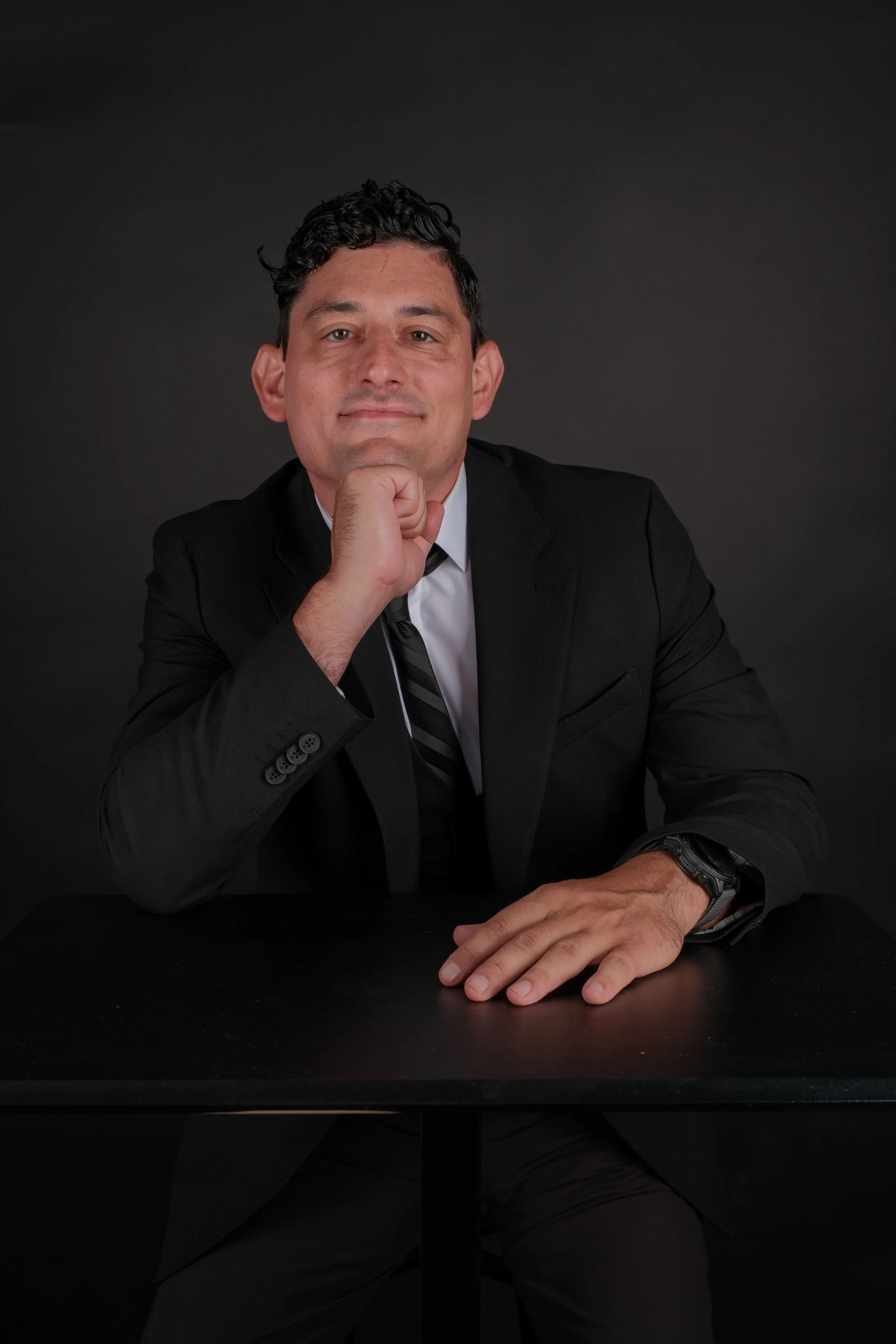 Author Alex Rodino posing in a black suit at a studio desk during a professional photoshoot.
