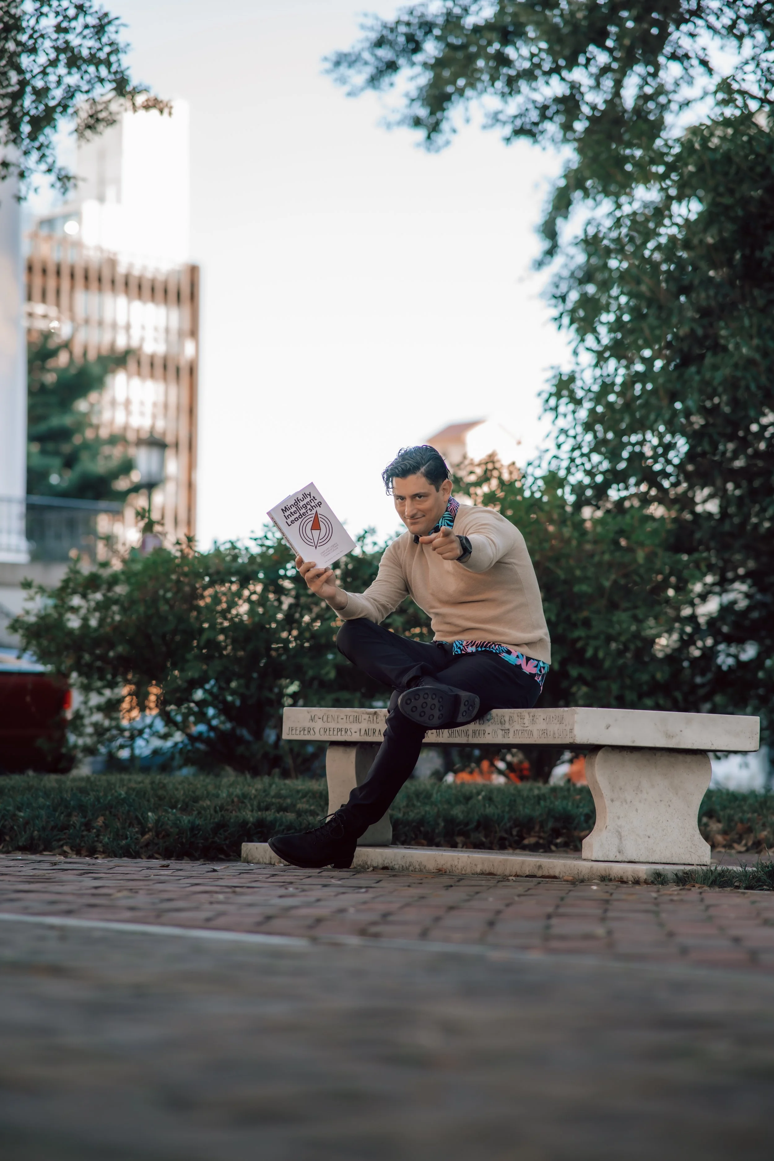 Alex Rodino holding Mindfully Intelligent Leadership book while pointing toward the viewer in an outdoor author portrait