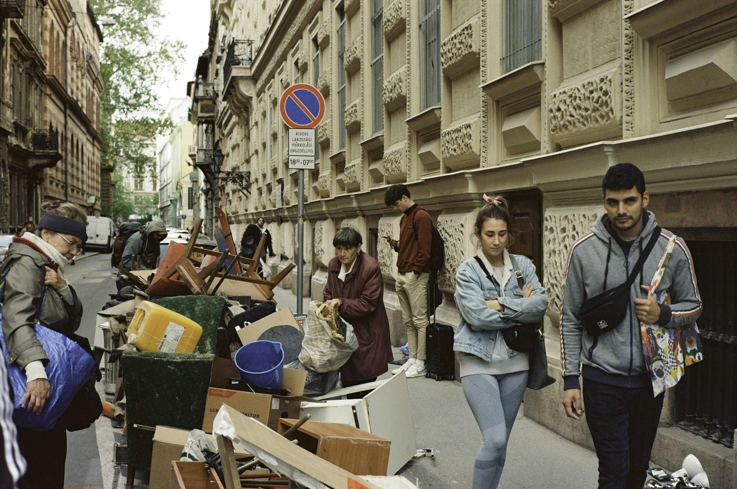 People on a city street with discarded furniture and belongings, some waiting or browsing