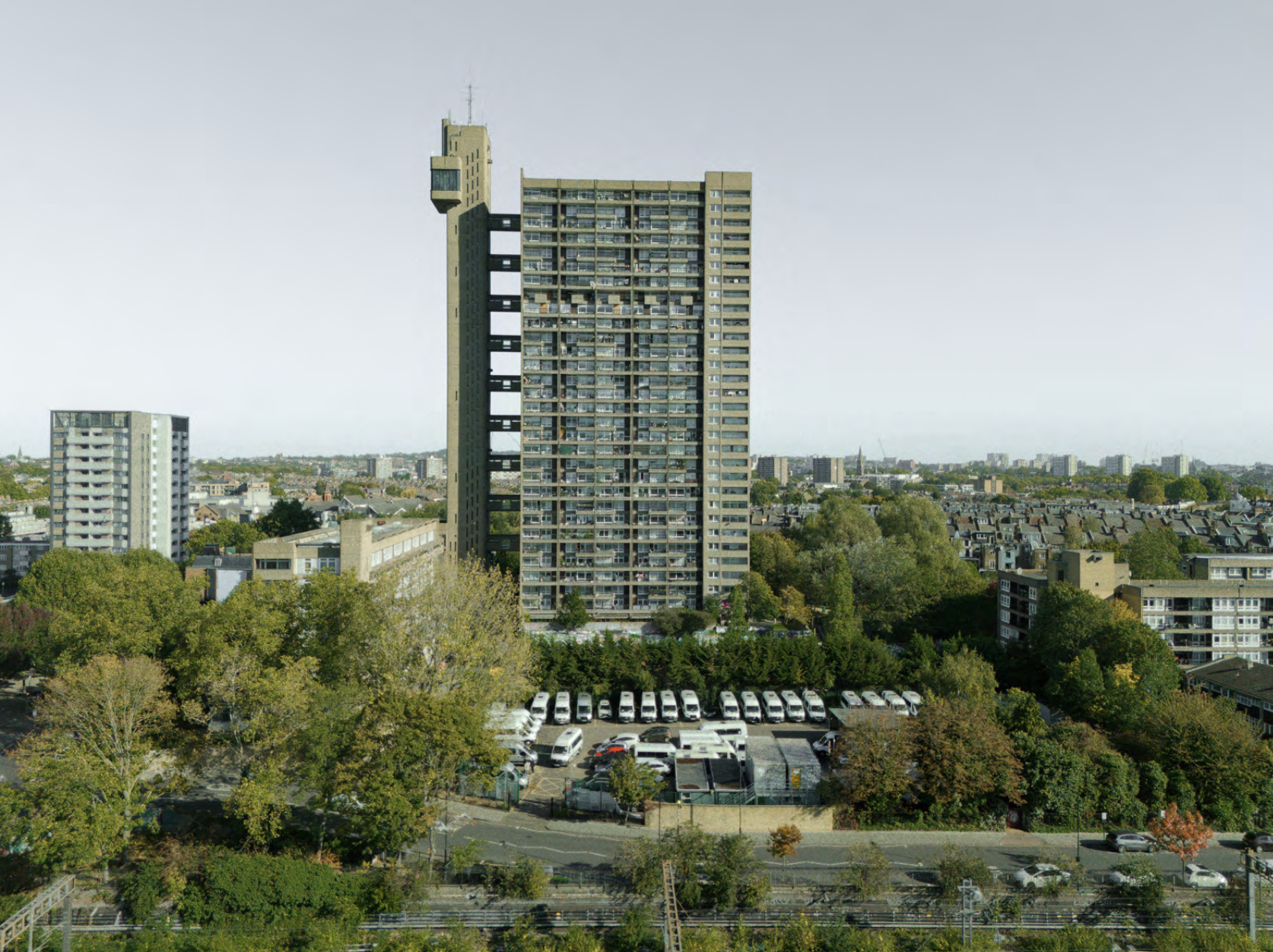 Tall residential apartment building in a cityscape with trees and parking lot in foreground.