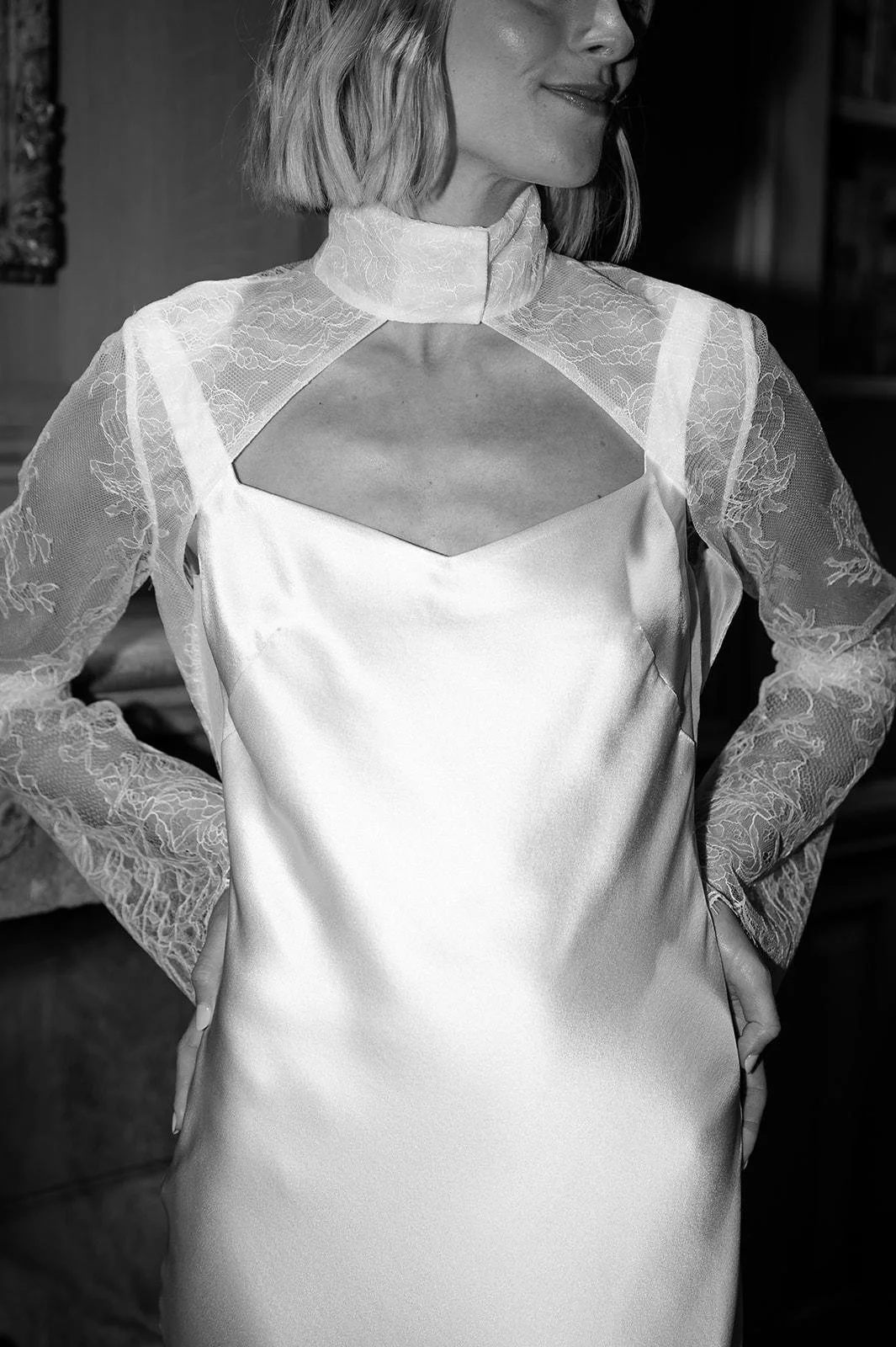 A woman wearing a satin dress with lace sleeves and a high neckline with a cutout design.