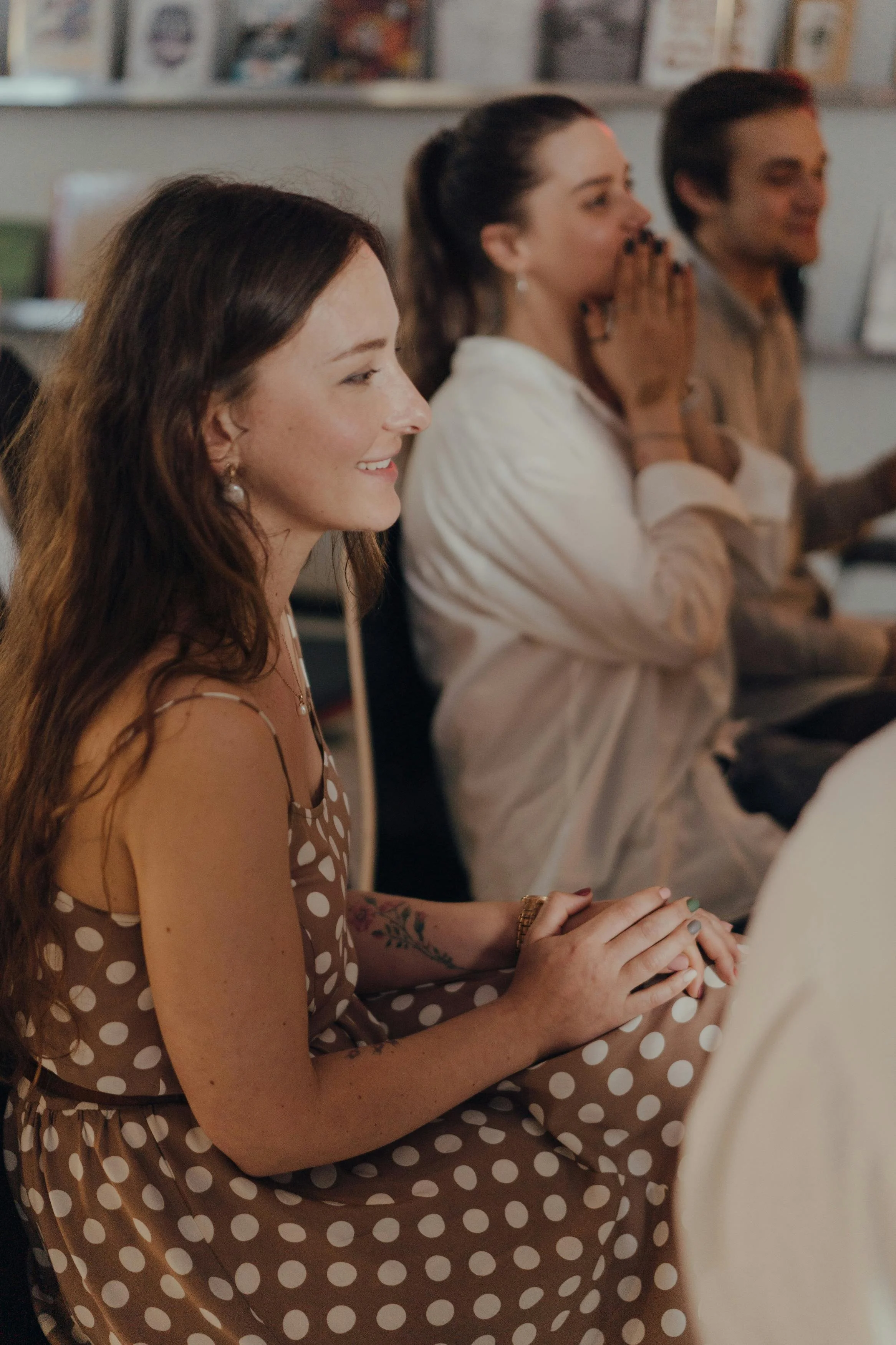 A group of people sitting in a row, smiling and attentive during an indoor event or presentation.
