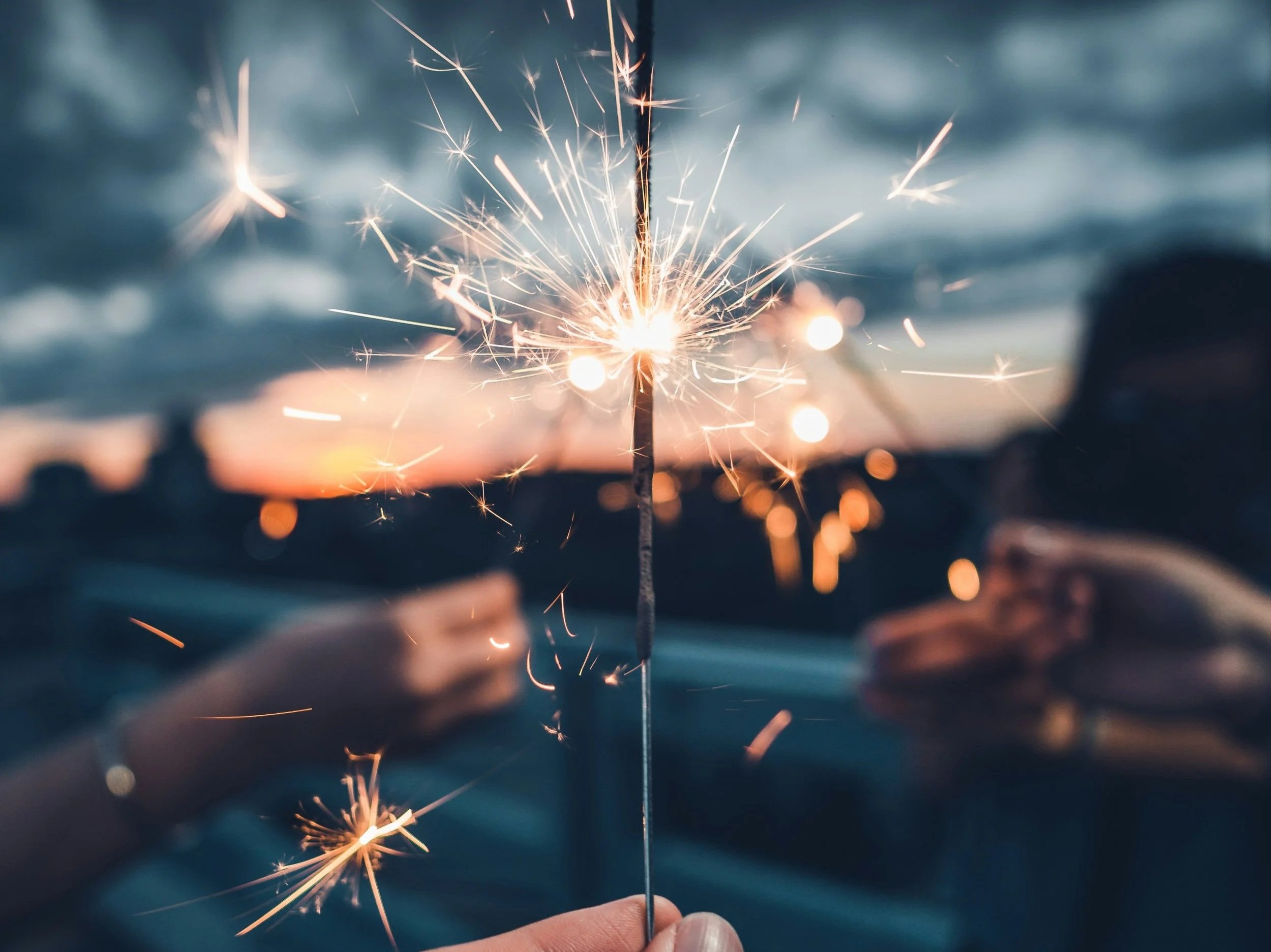 People holding sparklers at sunset on a beach.