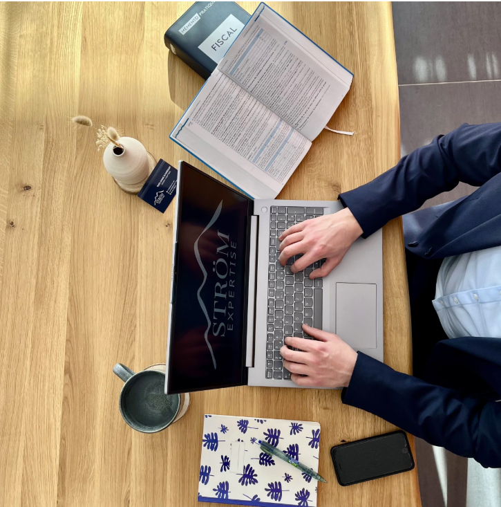 Une personne qui travaille sur son PC vue d'en haut. Le PC a en fond d'écran le logo STRÖM EXPERTISE.