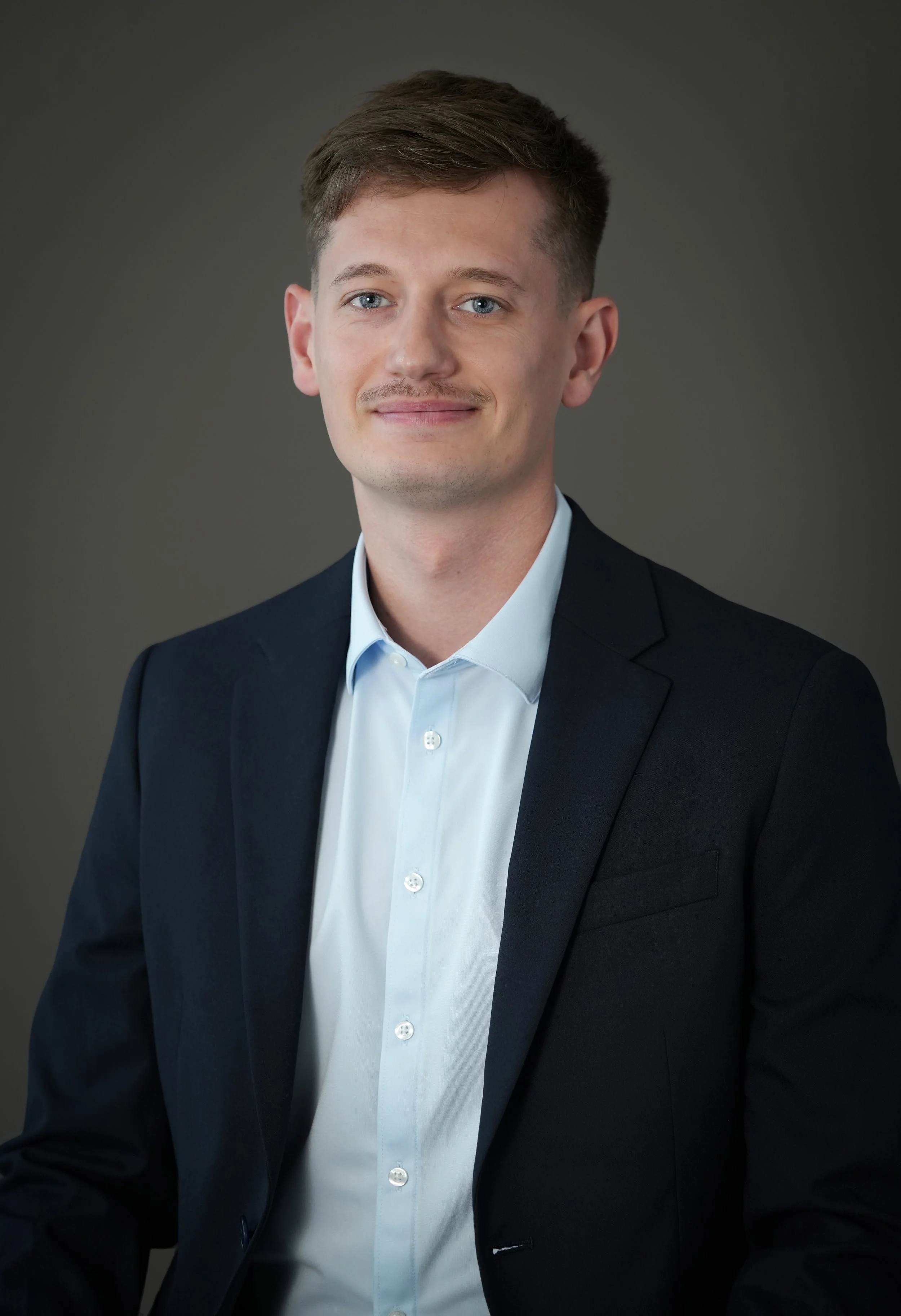 Une photo de Guillaume Schneider, l'expert-comptable de STRÖM EXPERTISE. Il est brun clair, avec les yeux bleus et une moustache. Il porte un costume bleu foncé avec une chemise bleu clair. Il fait très professionnel.
