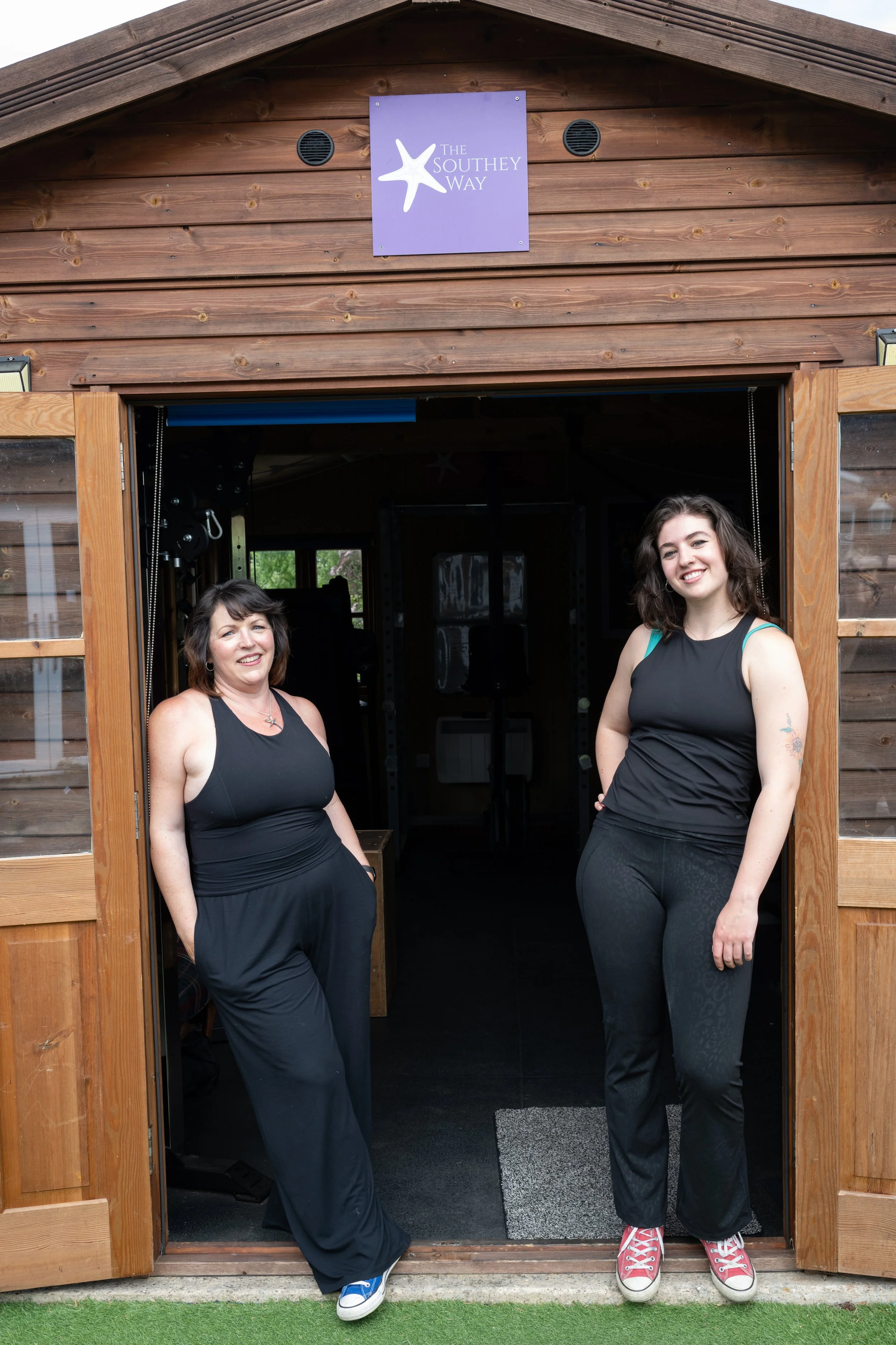 Co-directors Sara and Jenny standing in the doorway of a wooden building with a sign that reads 'The Southey Way' and a starfish logo above the entrance.