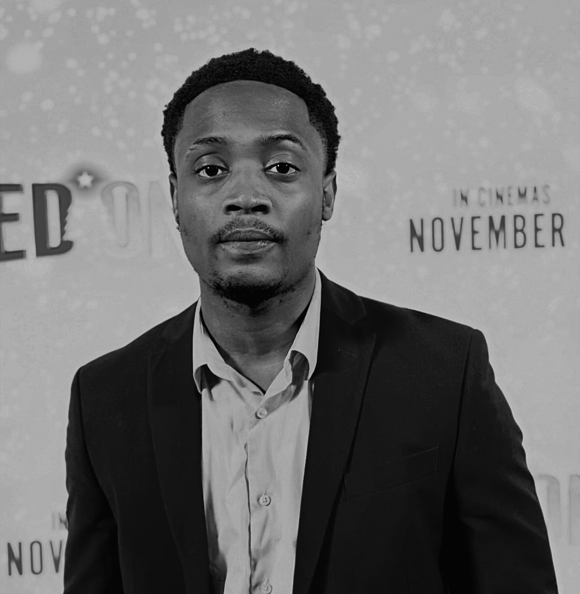 A man in a suit standing in front of a backdrop with text about the month of November.