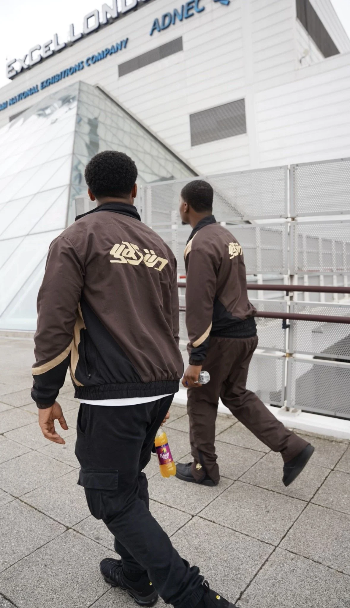Two men in brown and black jackets walking past the Xcel Energy Center, home of the Minnesota Wild, a sports arena.