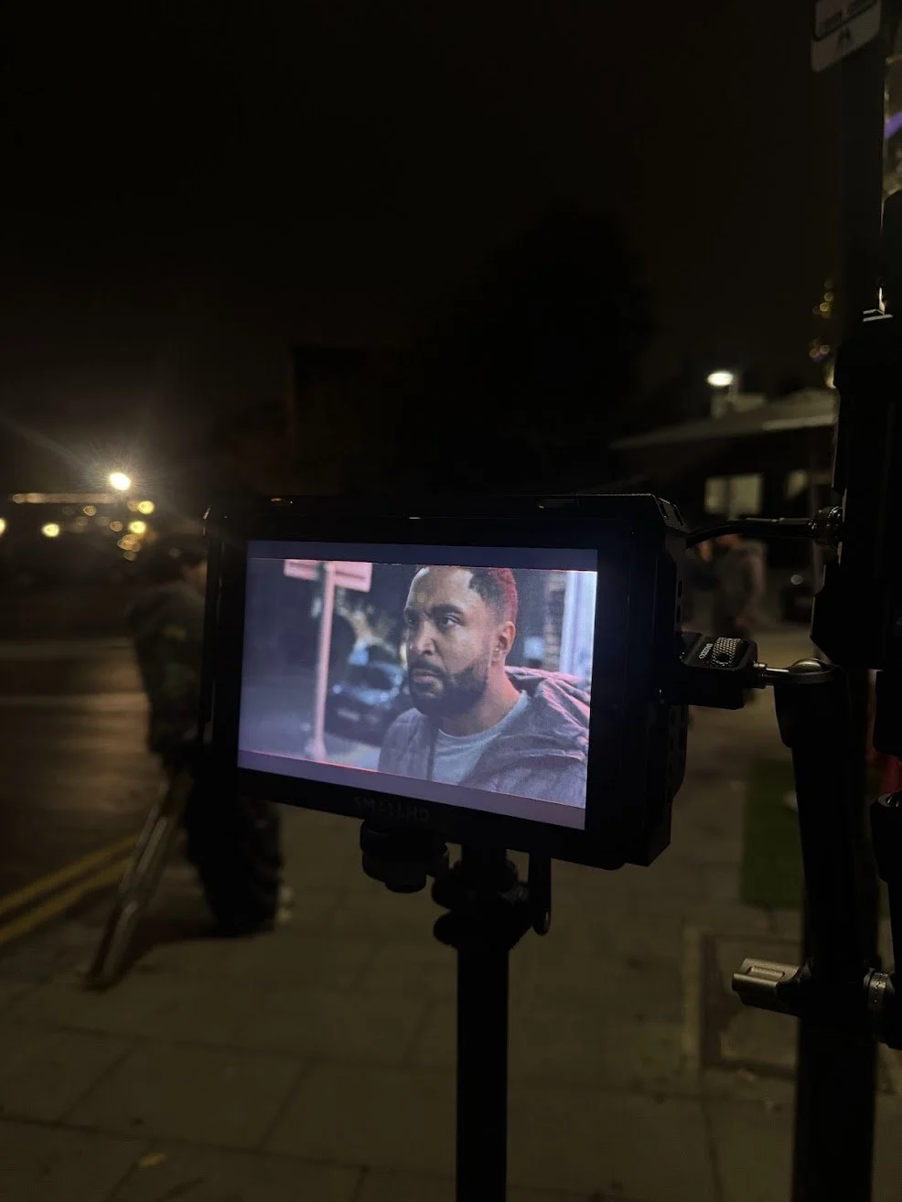 Film production scene at night, with a camera monitor showing a close-up of a man's face.