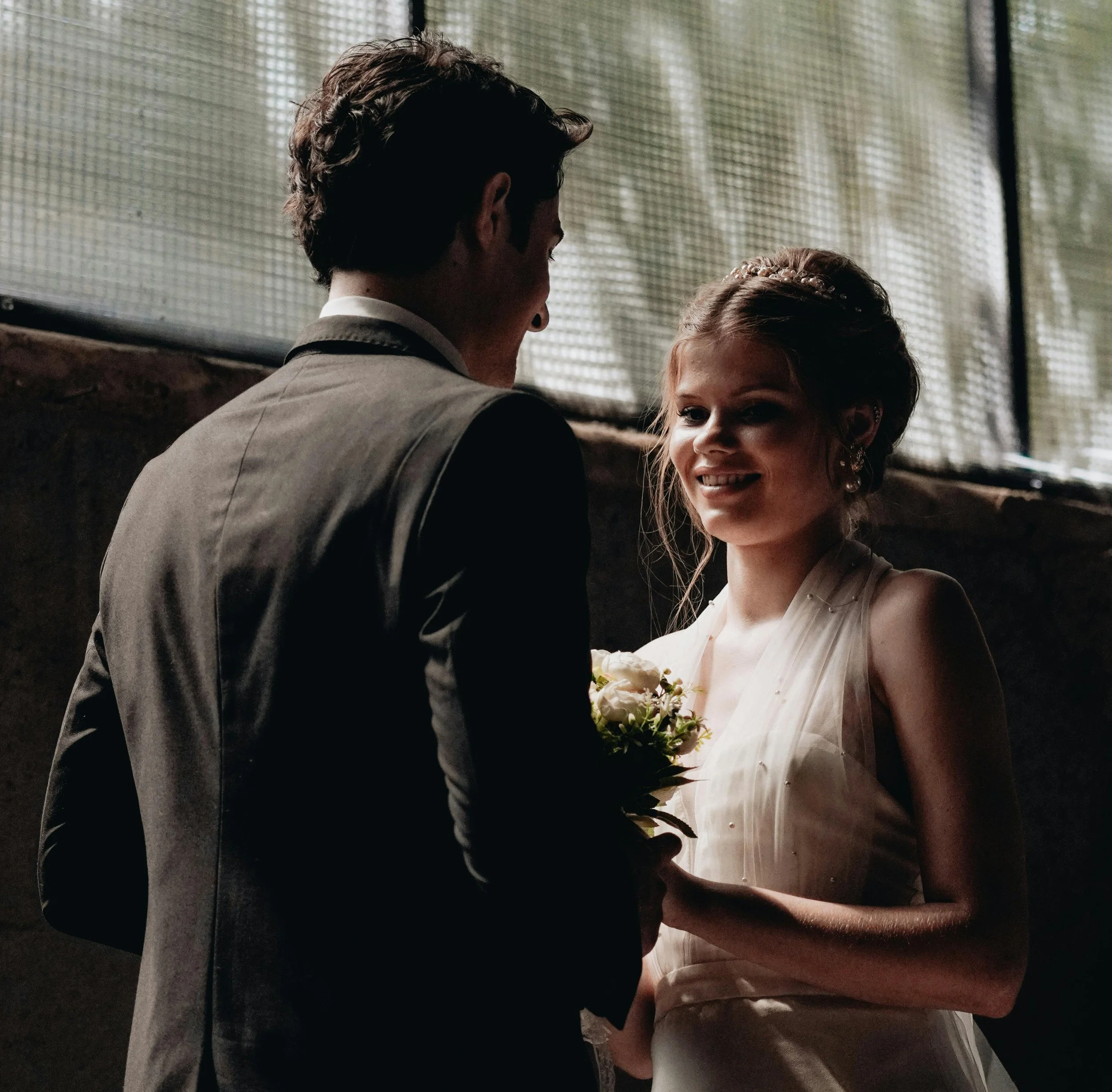 A bride and groom holding hands during their wedding, with the bride smiling and holding a bouquet of flowers.