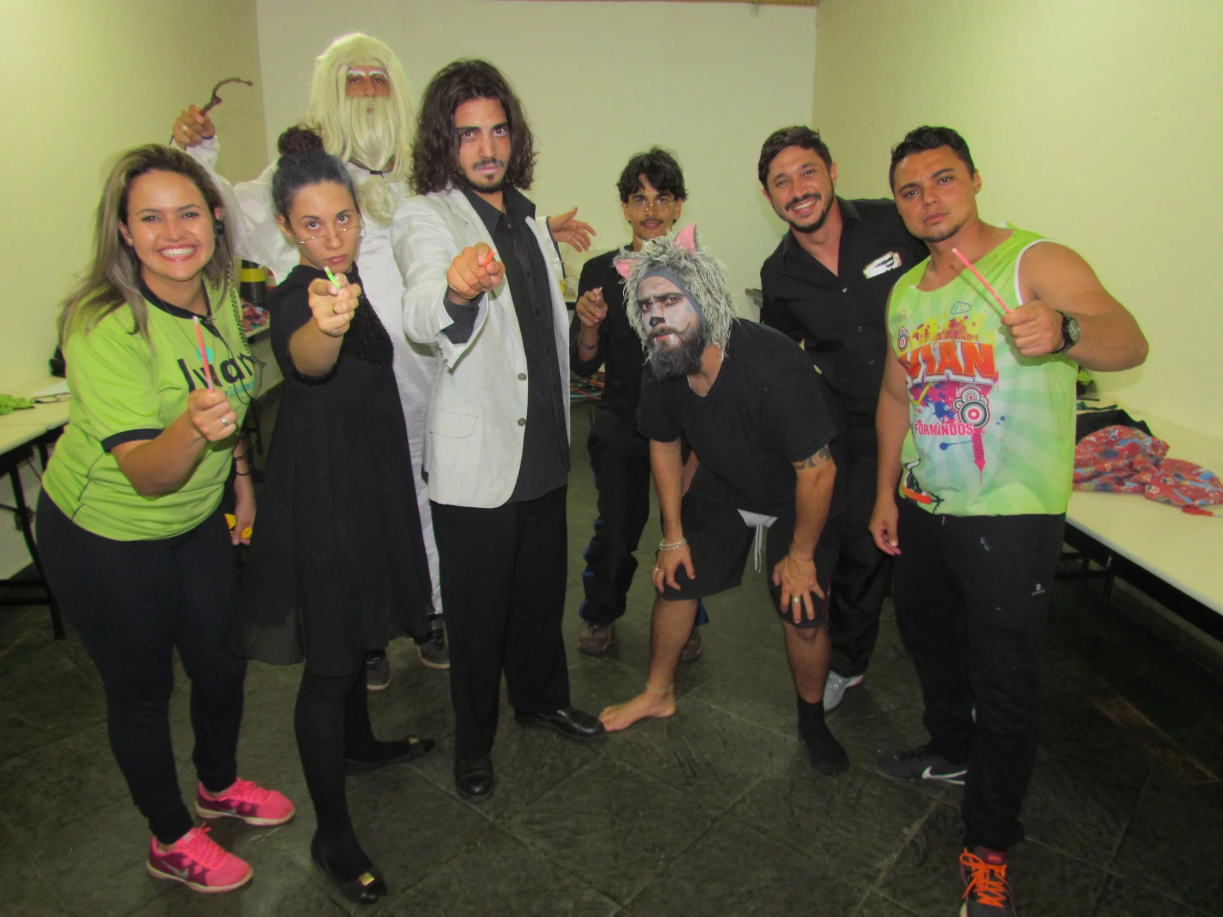 Grupo de pessoas em uma festa de fantasia, com maquiagem e roupas diferenciadas, sorrindo e fazendo pose, em ambiente interno com paredes verdes.