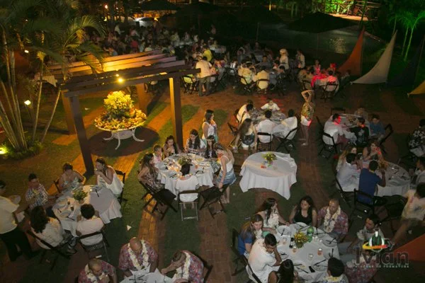 Jantar ao ar livre com várias mesas e convidados, iluminação suave e decoração acolhedora. Pacote de eventos noturno.