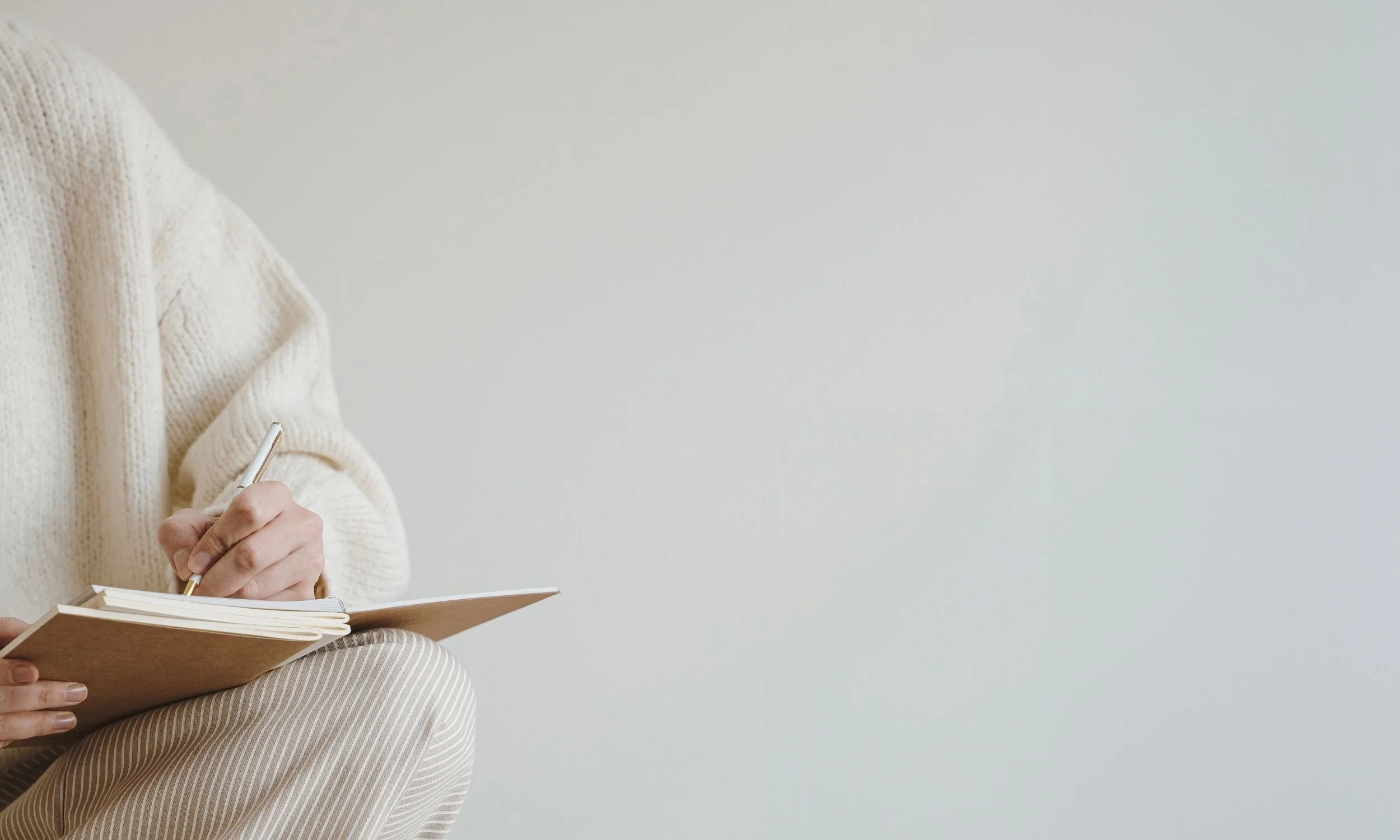 A professional in a cream sweater writing in a notebook, symbolising the thoughtful, reflective pacing of a strategic therapeutic or coaching engagement.