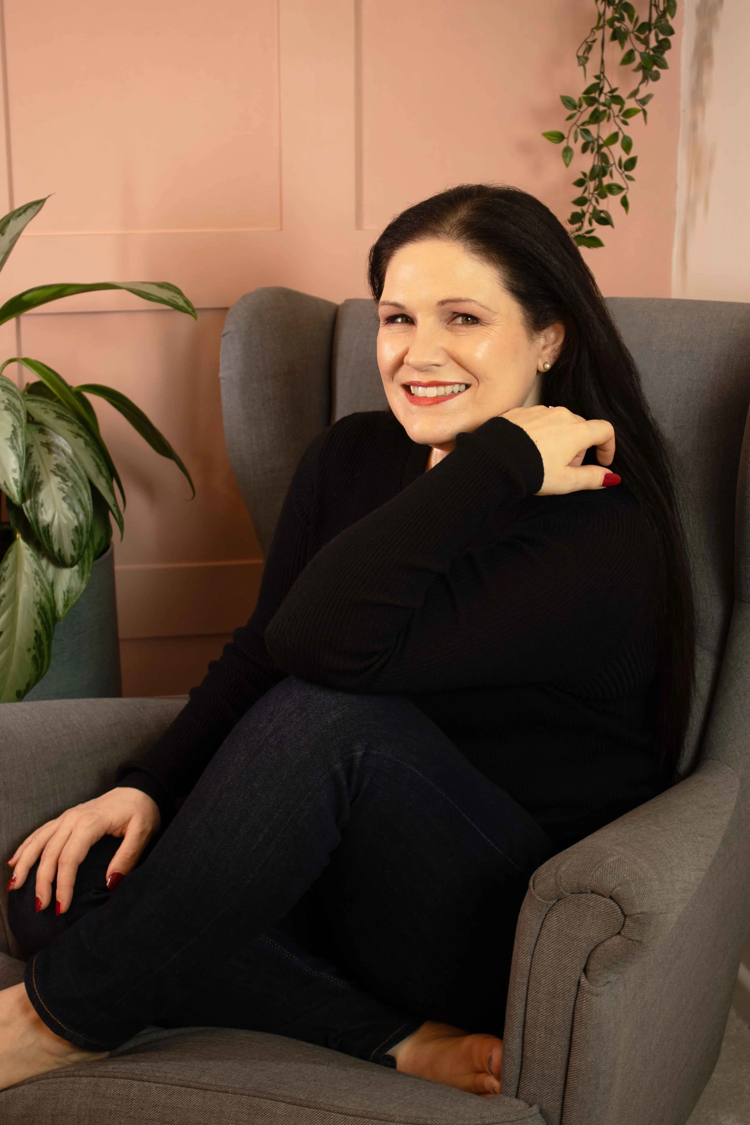 Clare, a cognitive behavioural hypnotherapist and Life Coach based in Andover, Hampshire, UK, sitting comfortably in a calm peach-toned therapy room, offering a warm and welcoming presence.