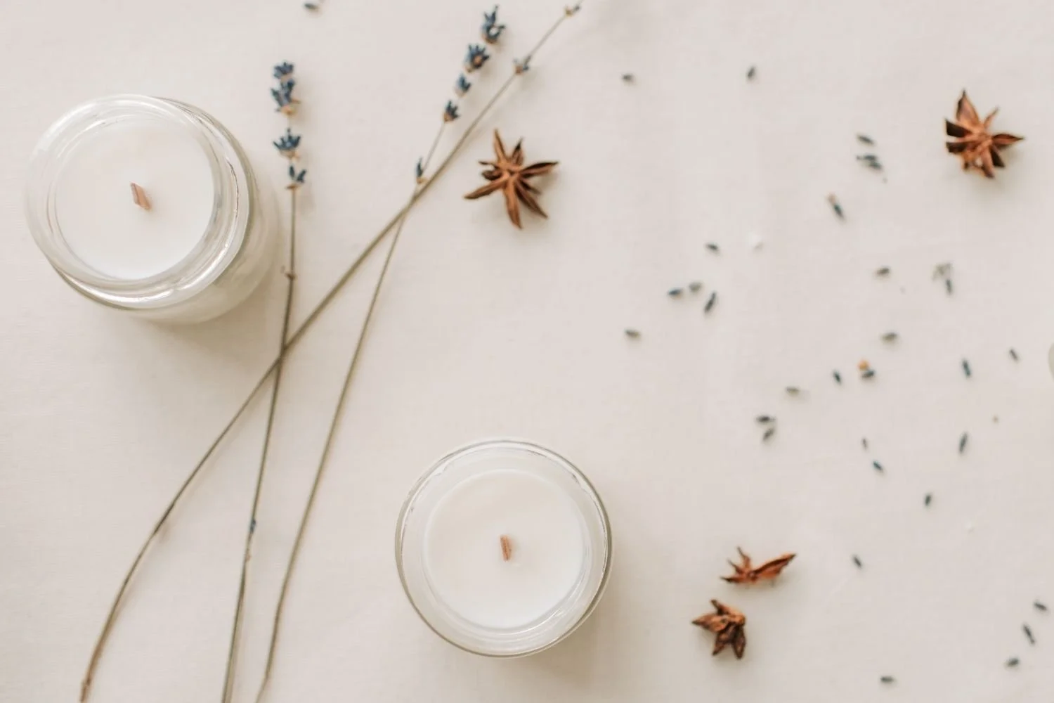 Two white candles in glass holders with dried lavender and star anise on a white surface representing emotional steadinesss and a structured approach to stress management.
