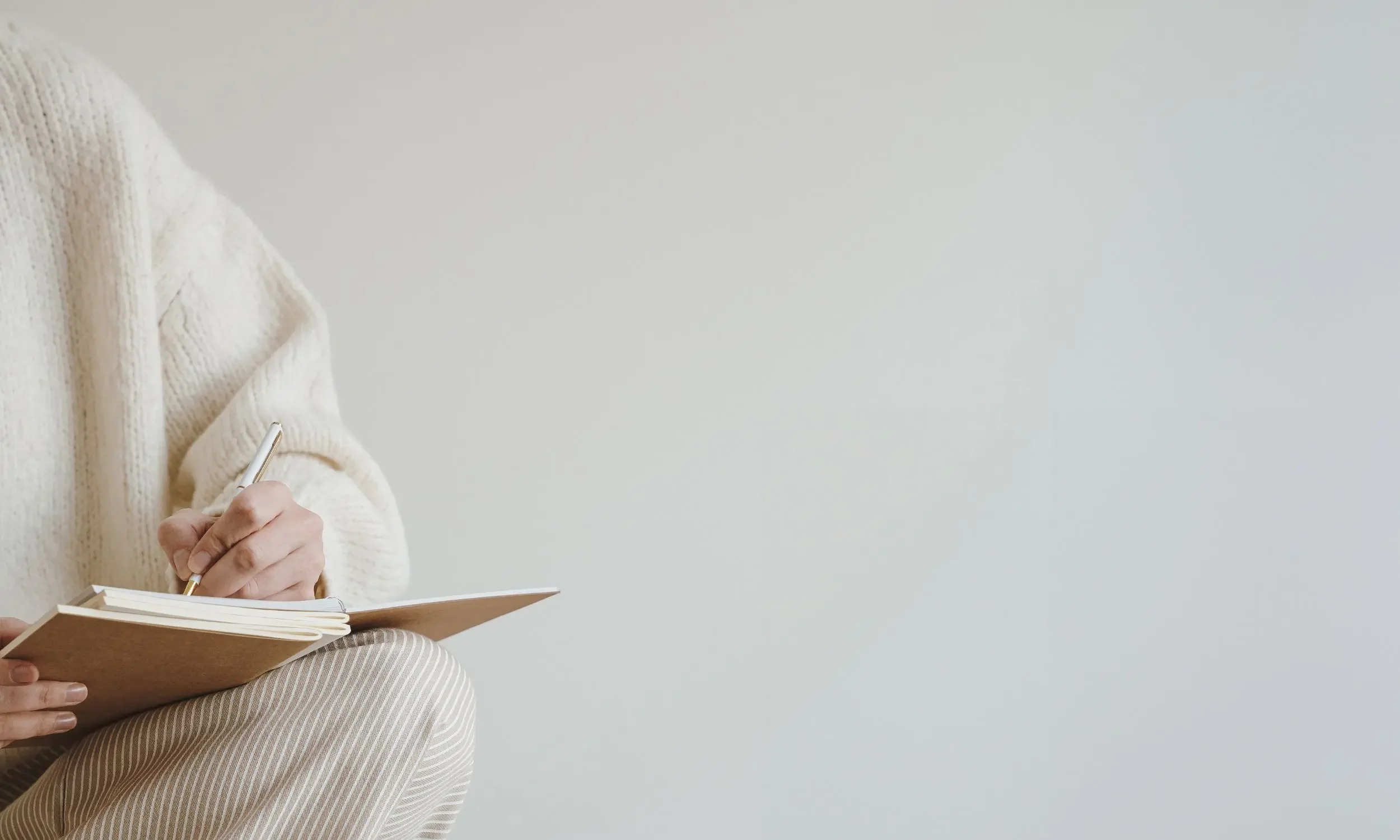 A professional in a cream sweater writing in a notebook, symbolising the thoughtful, reflective pacing of a strategic therapeutic or coaching engagement.