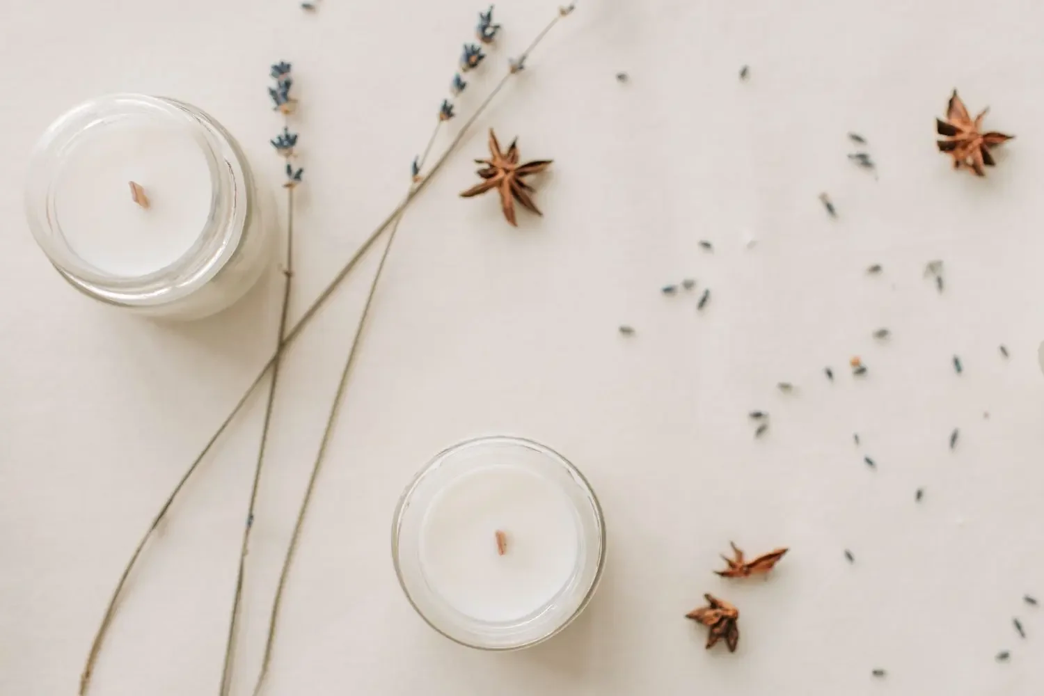 Two white candles in glass holders with dried lavender and star anise on a white surface representing emotional steadinesss and a structured approach to stress management and sleep anxiety.
