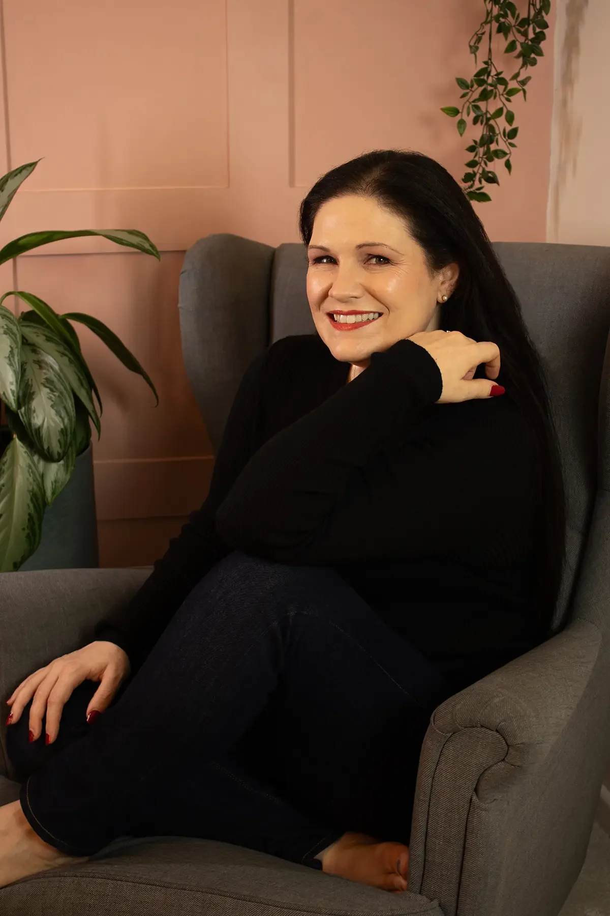 Clare, a cognitive behavioural hypnotherapist and Life Coach based in Andover, Hampshire, UK, sitting comfortably in a calm peach-toned therapy room, offering a warm and welcoming presence.