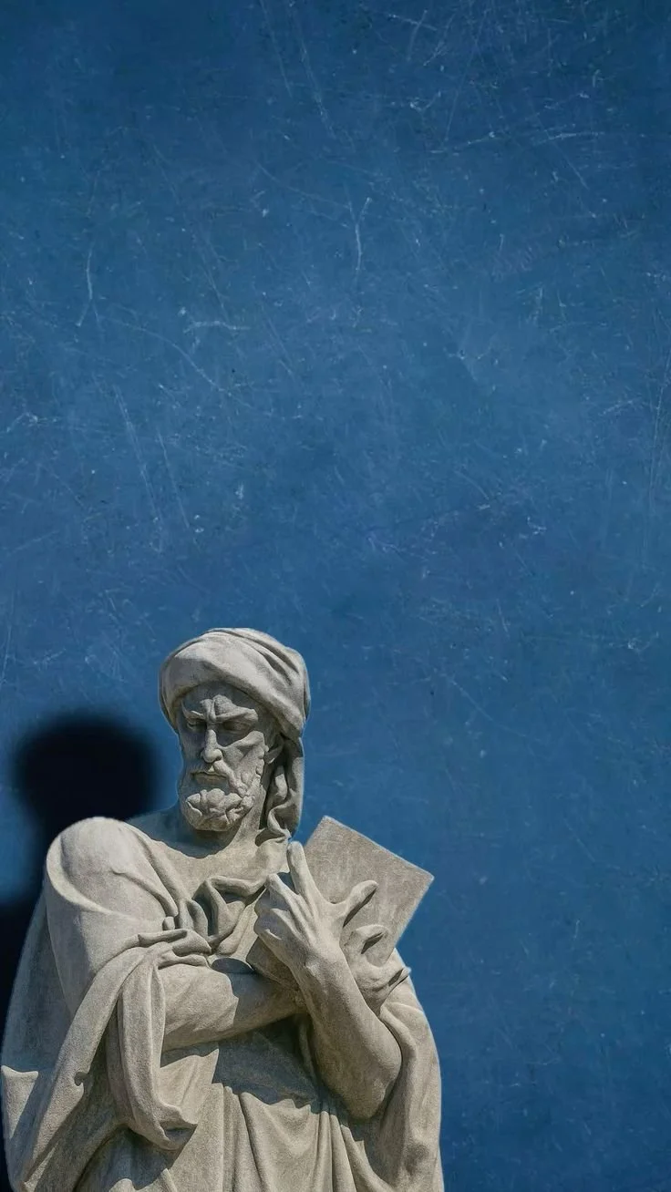Statue of a bearded man with a turban, reading a book, against a blue background.