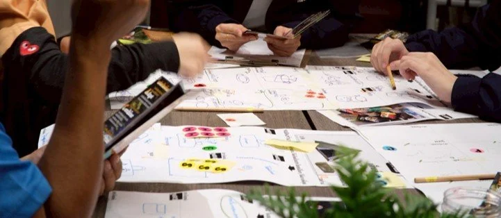 People working on papers and sketches on a table in a meeting or collaborative setting.