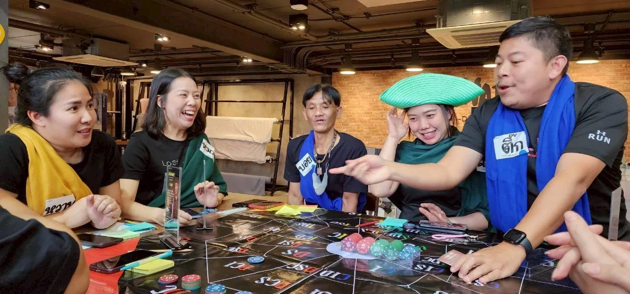 Group of people playing a board game, smiling, with some wearing colorful accessories and headgear.