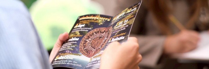 Person holding and reading a dark-colored brochure or leaflet.