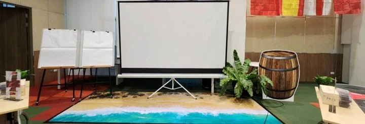 Indoor event setup with a projection screen, plants, and various decorative items.