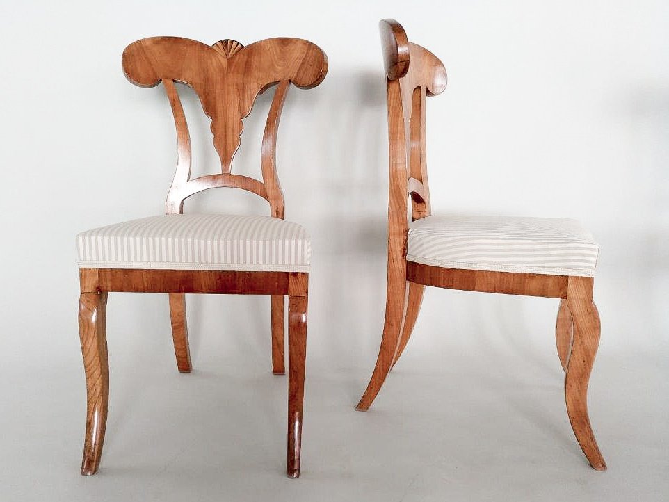 Zwei elegante Holzstühle mit gepolsterten Sitzflächen, einer mit hoher Rückenlehne in Herzform und der andere mit geschwungener Rückenlehne, vor einem weißen Hintergrund.