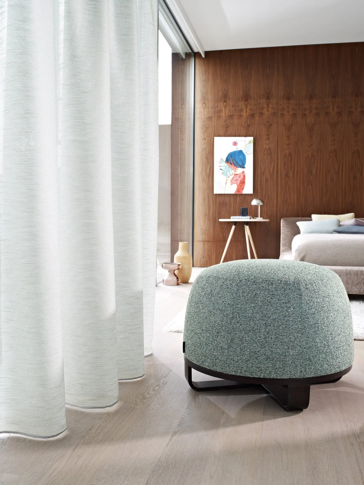 Moderner Wohnraum mit Holzvertäfelung, grauem Sofa, buntem Bild an der Wand, runder grüner Hocker, Vorhängen und Vasen.