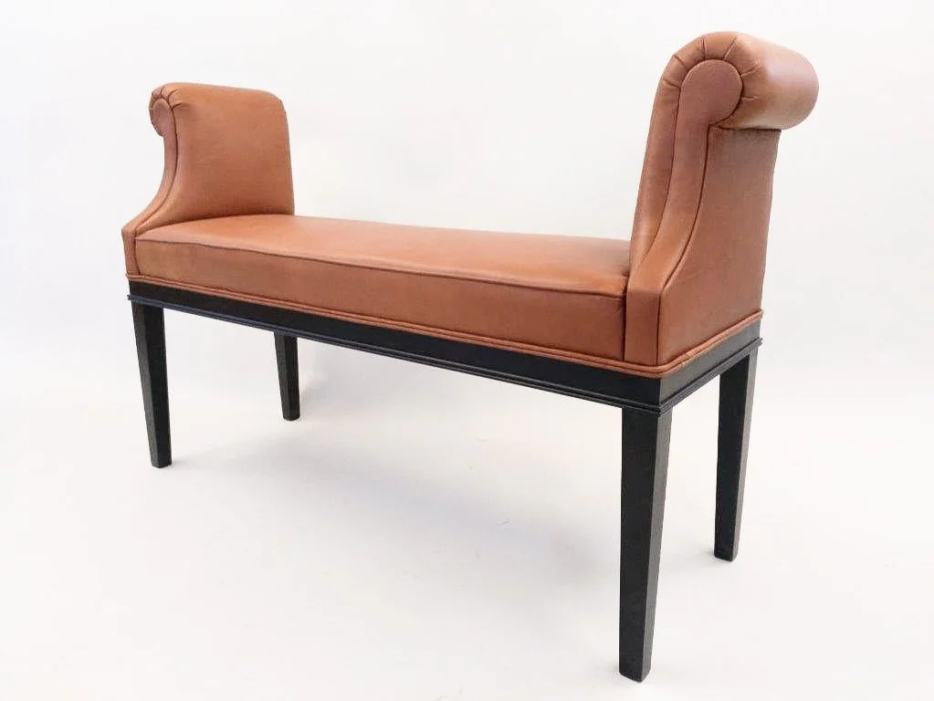 Ein stilvoller Hocker mit schwarzen Beinen und hellbraunem Lederbezug, inspiriert von einem alten britischen Design.