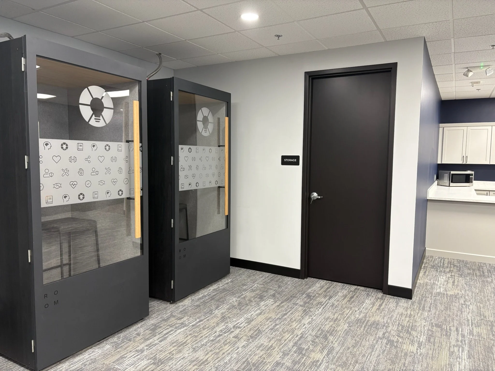 EOS sessions space in Ann Arbor, MI with Office waiting area with two glass-enclosed soundproof booths, a storage room door, and a small kitchenette in the background.