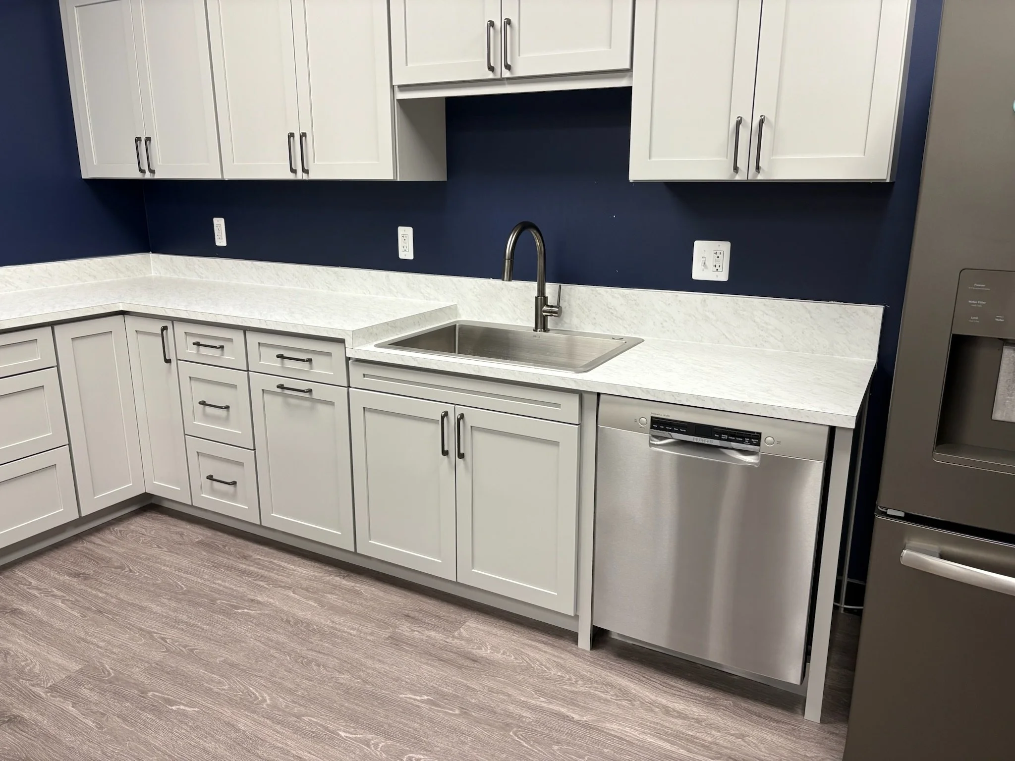 EOS sessions space in Ann Arbor, MI, with Kitchen with white cabinets, a stainless steel dishwasher, a white marble countertop, a sink with a modern faucet, a blue wall, and a stainless steel refrigerator.