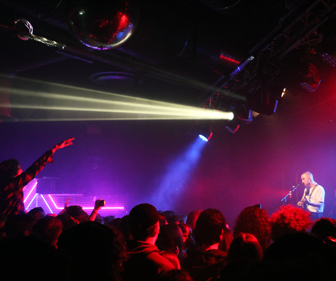 A live musical performance at a concert with colorful stage lights, an audience, and a singer playing guitar on stage.