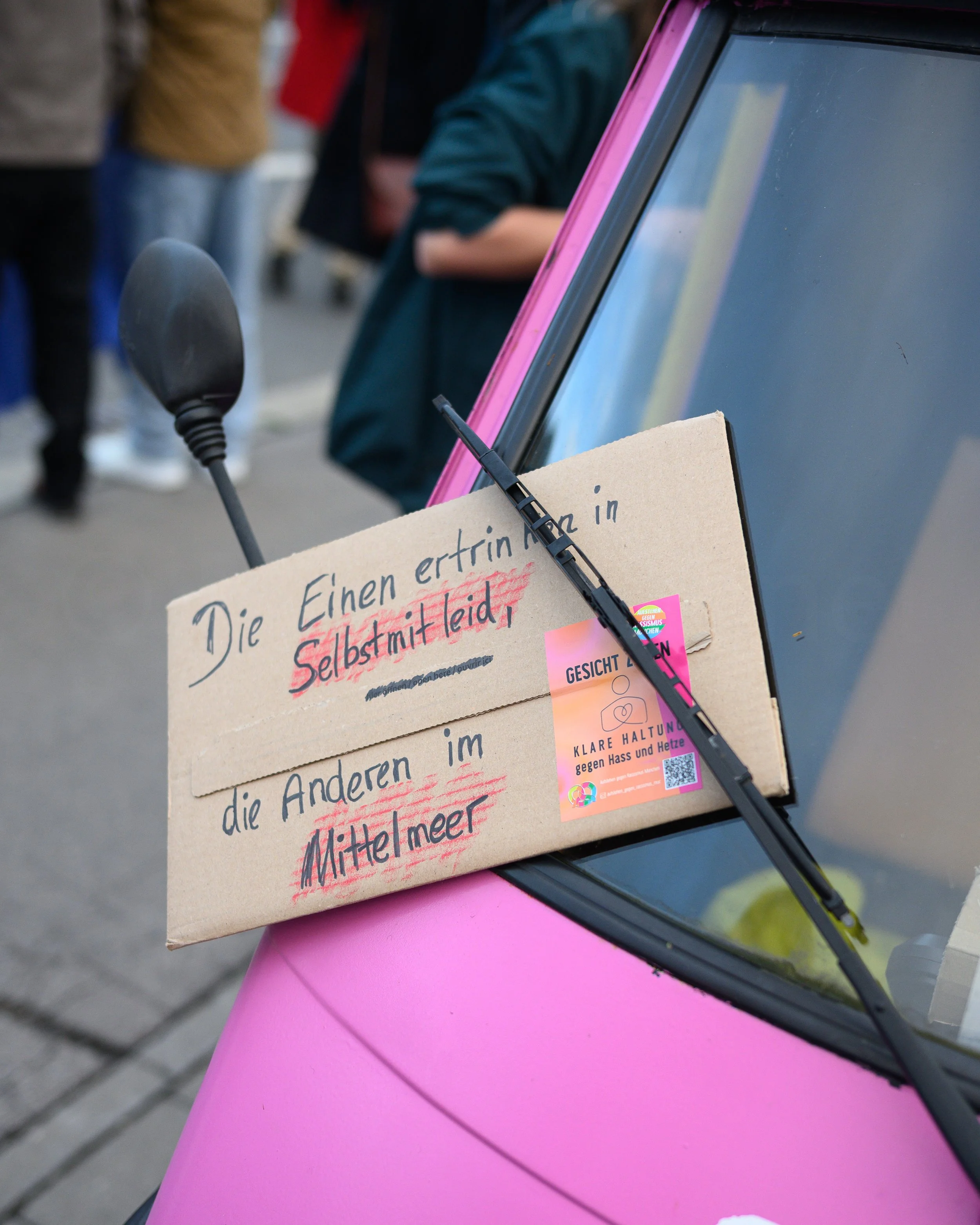 Ein Plakat und ein Zettel auf einem pinkfarbenen Fahrzeug, mit deutschen Texten, die sich gegen Hass und Hetze im Mittelmeer richten.