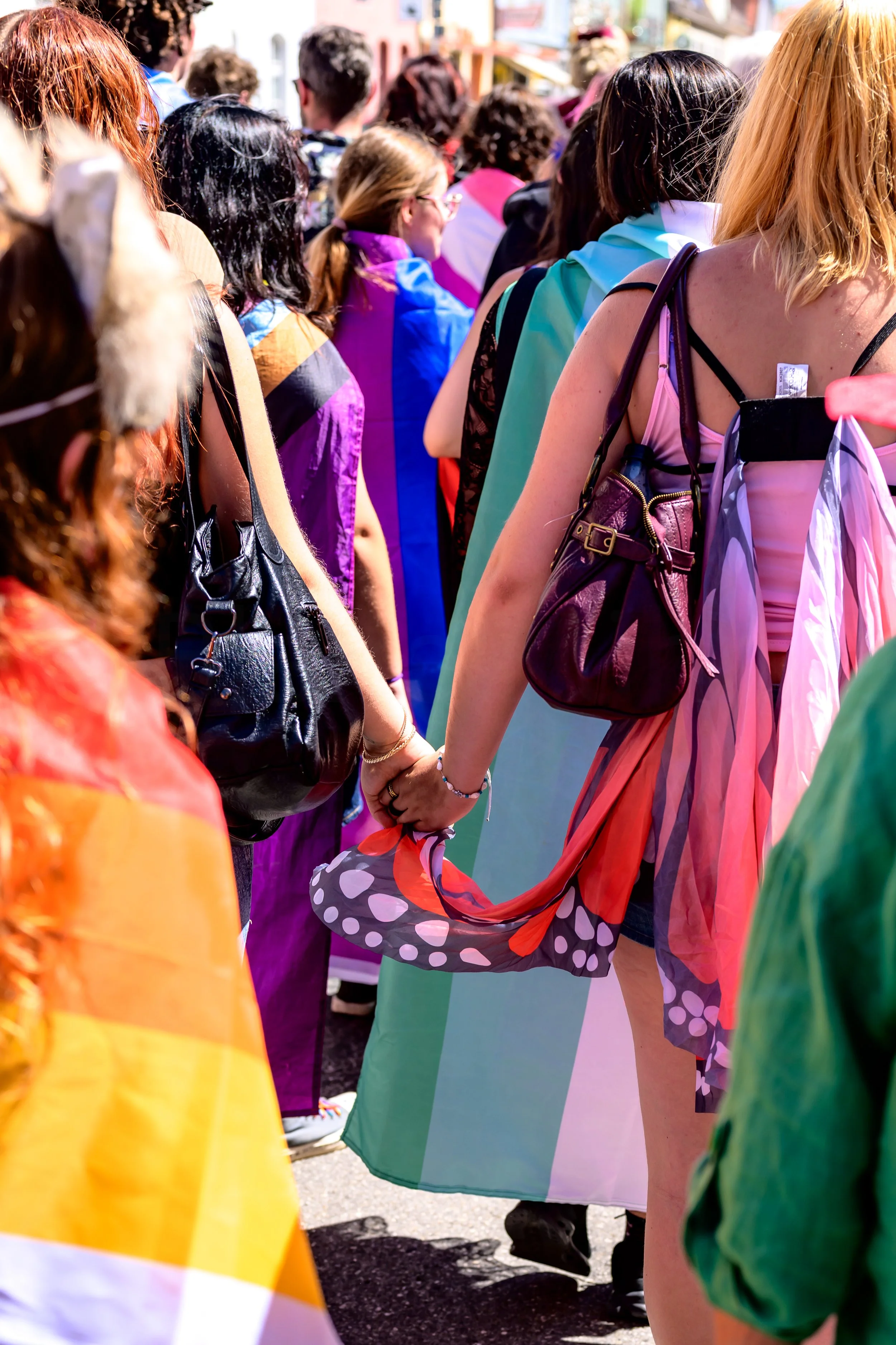 Menschen bei einer LGBTQ+-Demonstration, einige halten Regenbogenflaggen, in bunten Outfits. Es findet wahrscheinlich eine Pride-Parade oder eine ähnliche Veranstaltung statt.