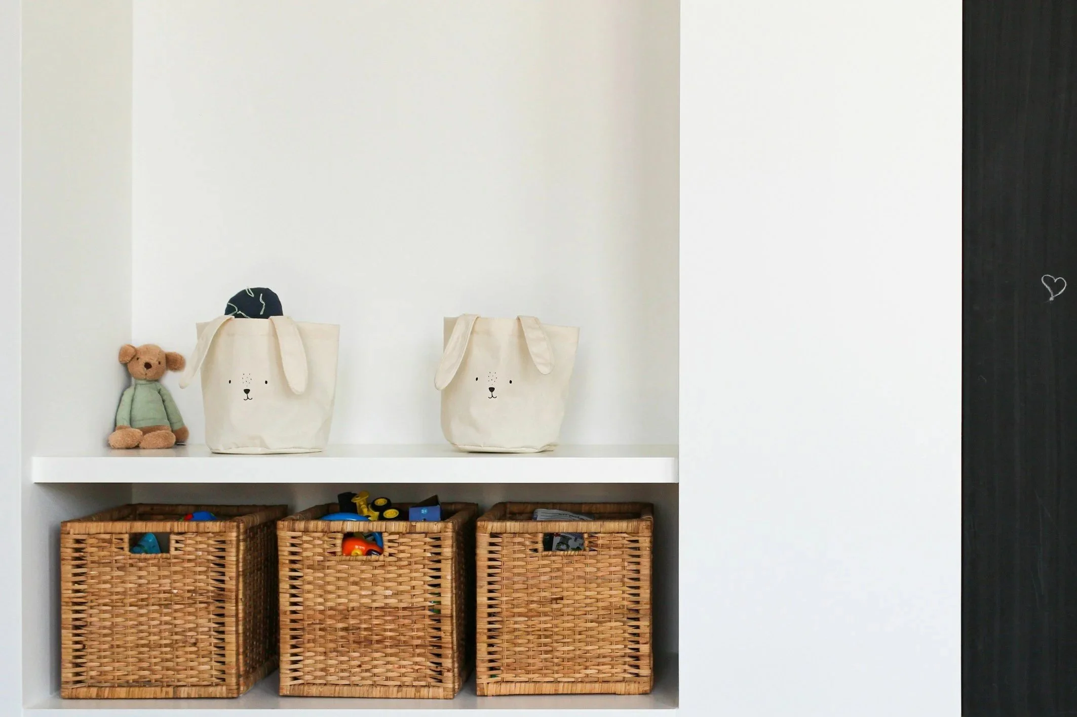 Witte muur met knuffels op een witte plank, onder drie manden met speelgoed.