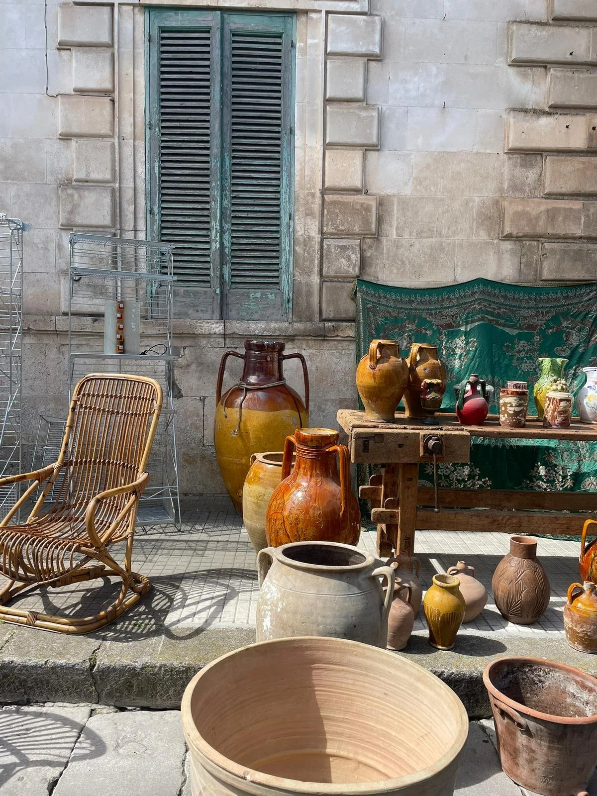 Tegeltassen, vazen en kramen met keramische potten en vazen buiten op straat, met een houten tafel en windscherm op de achtergrond.
