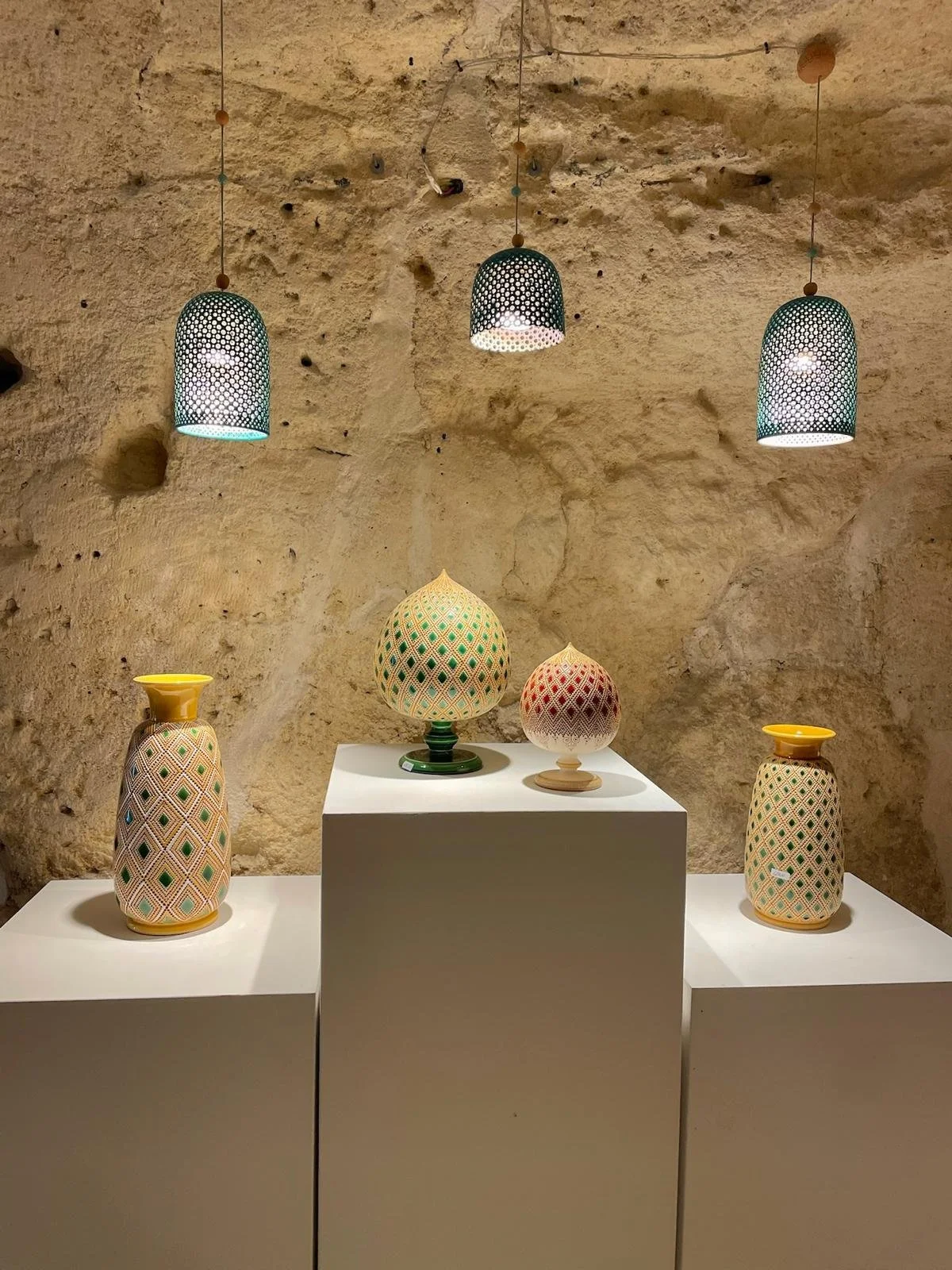 Decoratieve keramische vazen en bollen met geometrische patronen, uitgestald op witte kubusvormige voeten in een museum met een ruwe stenen muur.