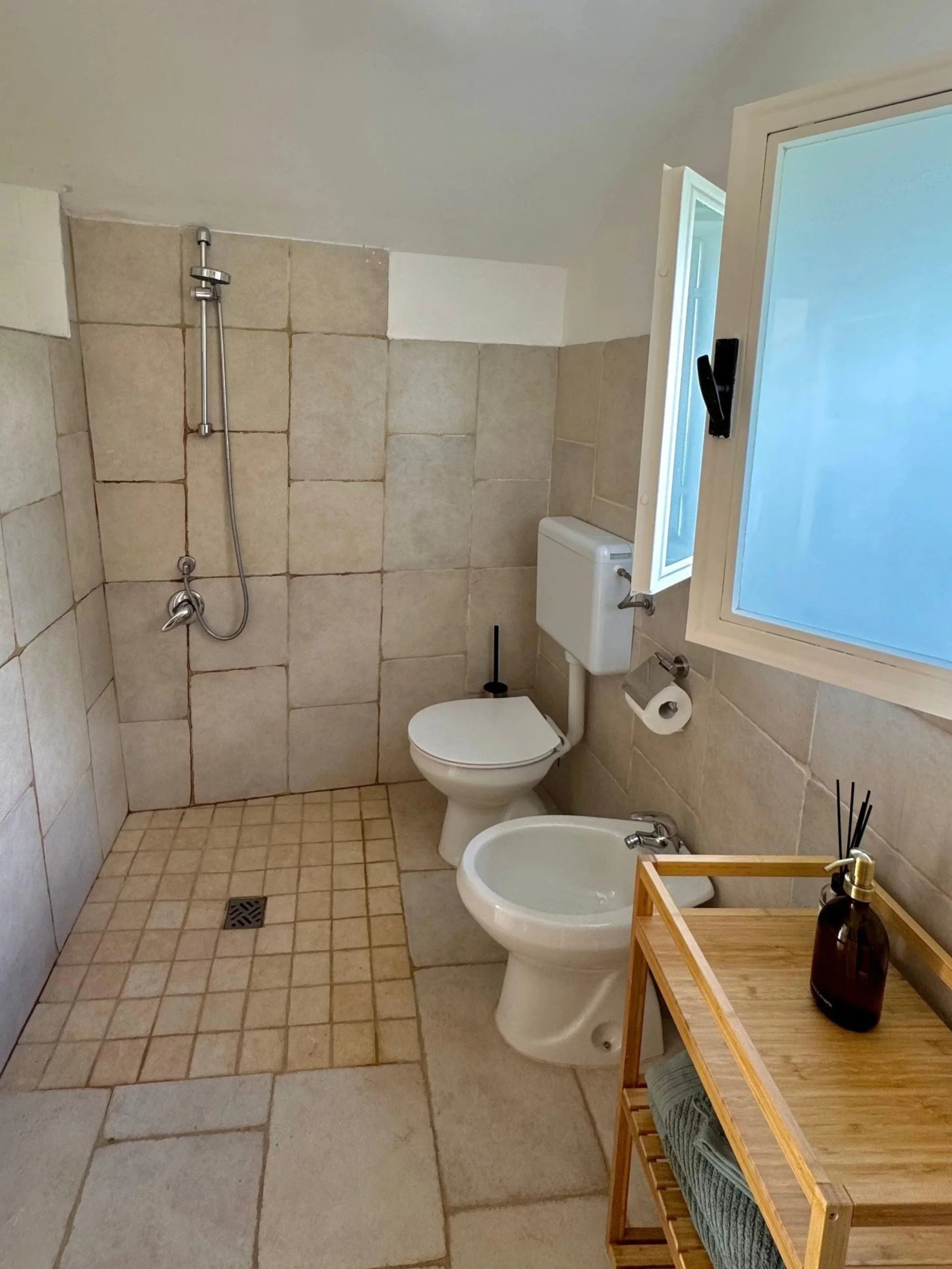 Een eenvoudige badkamer met een douche, toilet en een biertje op een houten plankje.