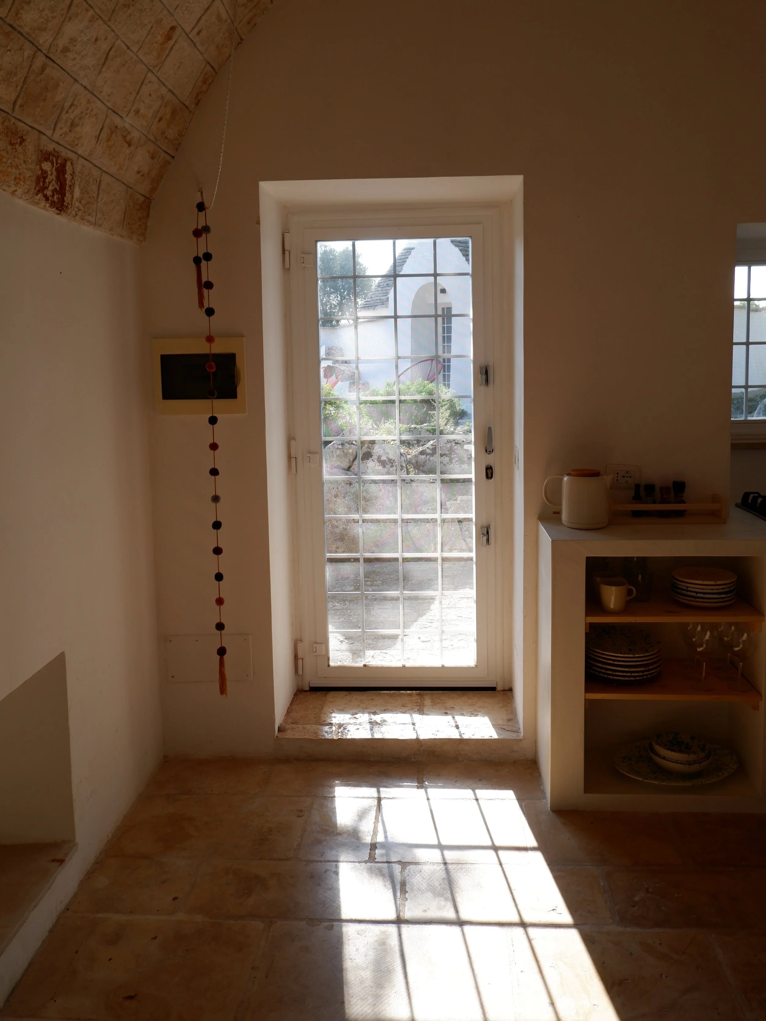 Binnenruimte met een deur naar buiten, zonnelicht en een kast met servies.