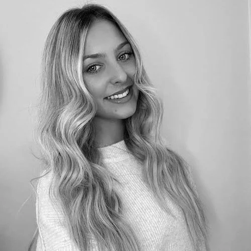 A young woman with long, wavy blonde hair smiling at the camera in black and white.