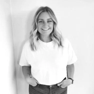 Black and white photo of a smiling young woman with wavy hair, wearing a casual t-shirt and jeans.
