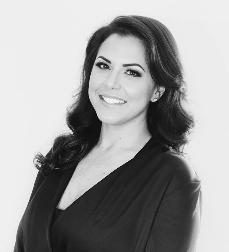 Black and white portrait of a woman with long, wavy hair smiling at the camera, wearing a dark blazer.