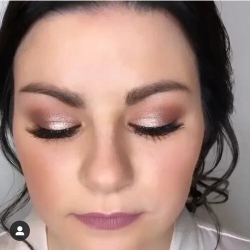 Close-up of a woman with makeup featuring shimmery eyeshadow, long eyelashes, and pink lipstick, with her eyes closed.