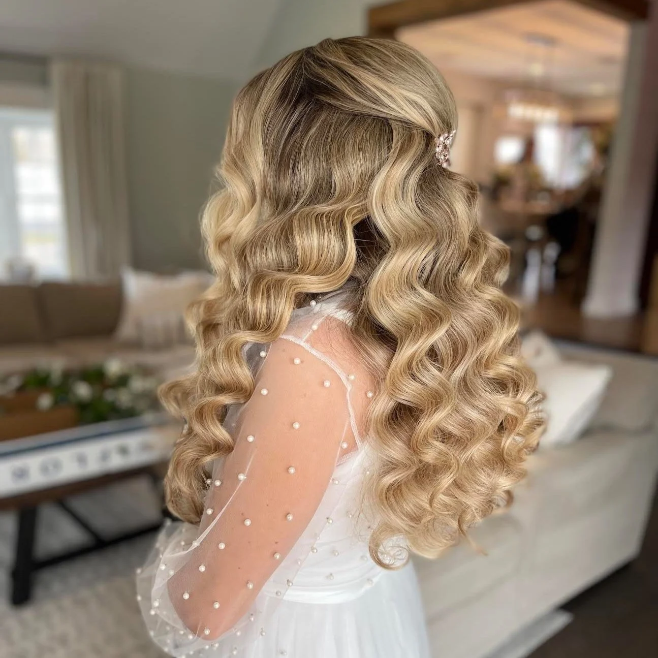 A woman with long, blonde, curly hair styled with a pearl hair accessory.