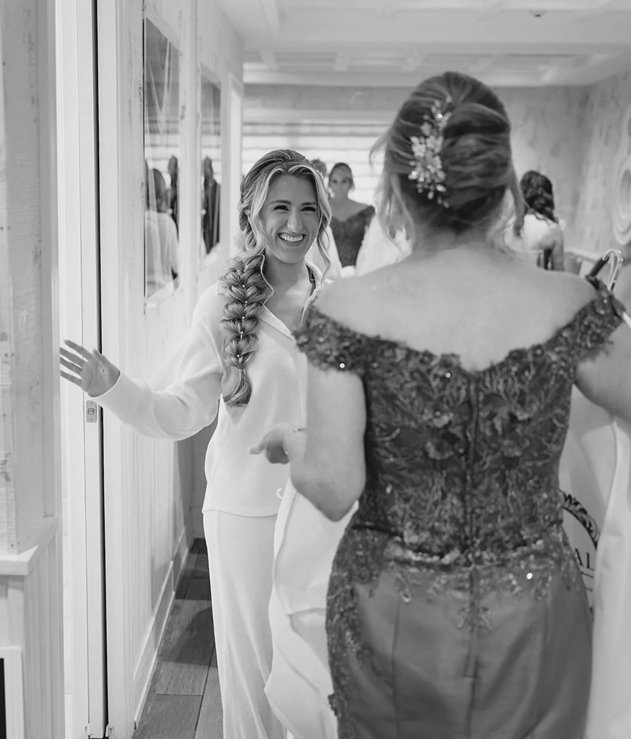 A woman in pajamas smiling and waving at another woman in an elegant dress during a joyful moment indoors.