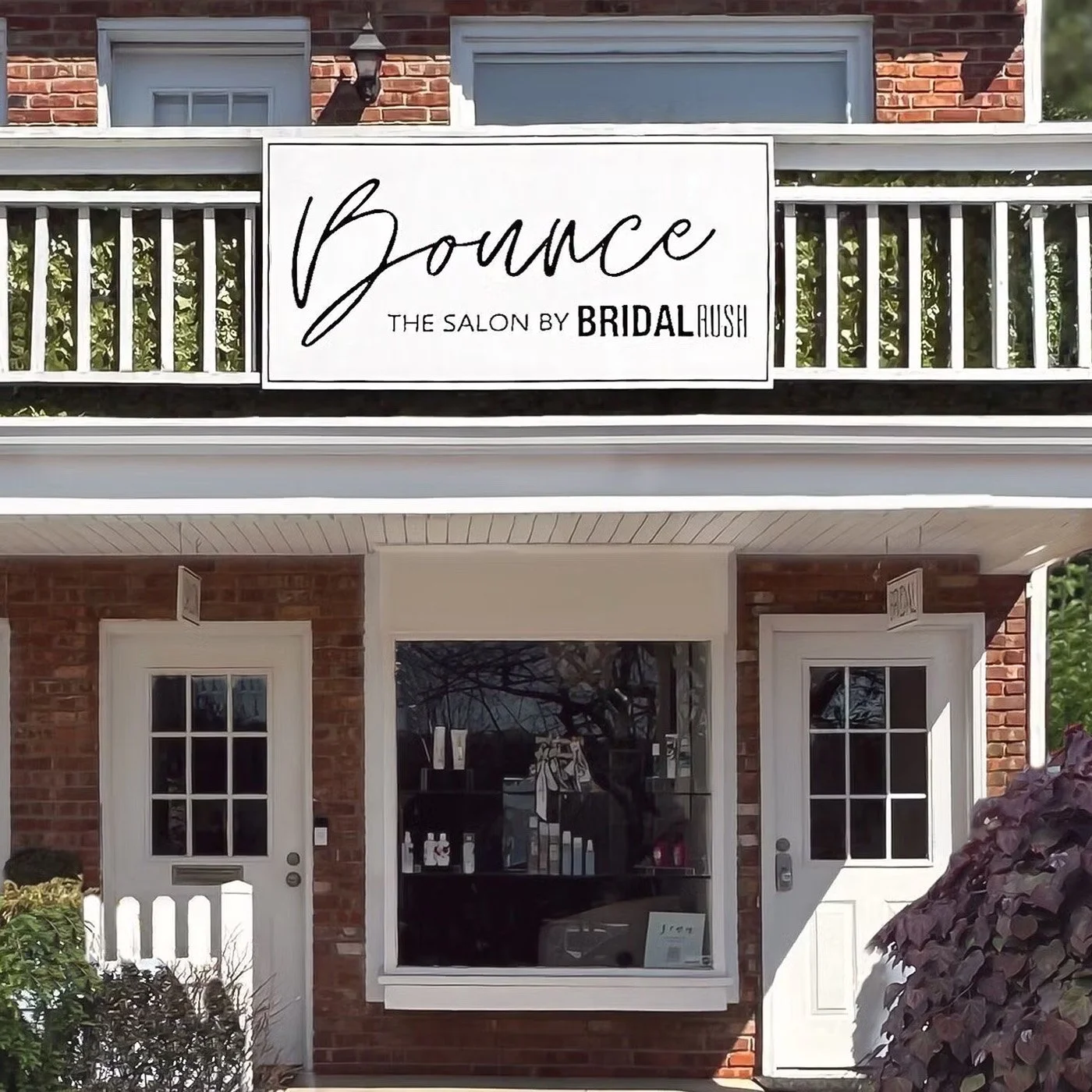 Exterior view of a brick building with a balcony, white doors, and windows. A large sign reads 'Bounce, the salon by Bridal Rush'.