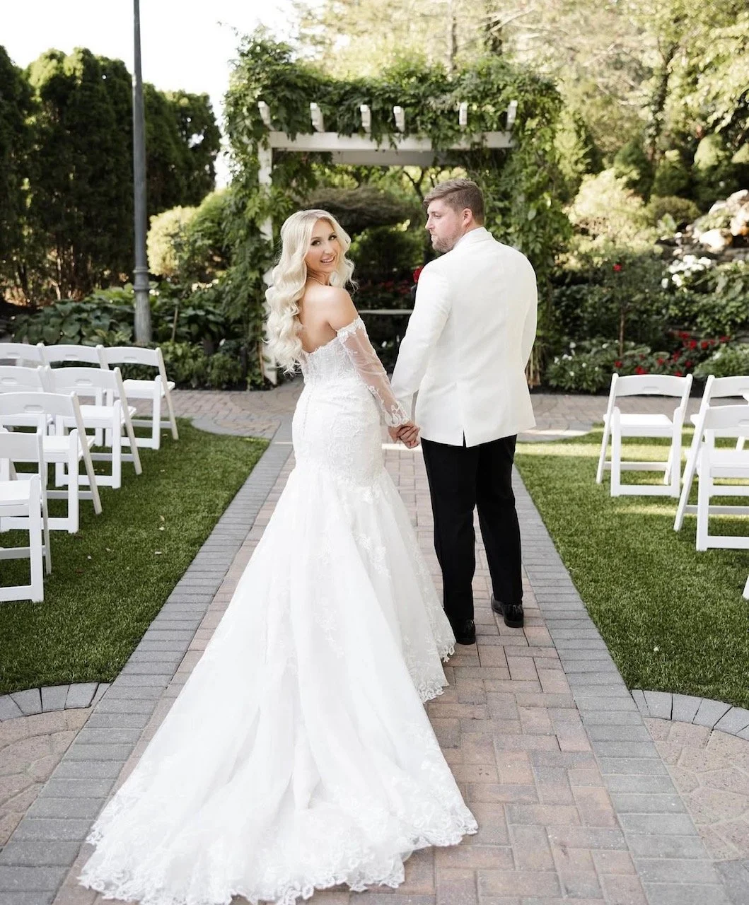 Bride and groom holding hands outdoors during wedding, with wedding arch and chairs in background